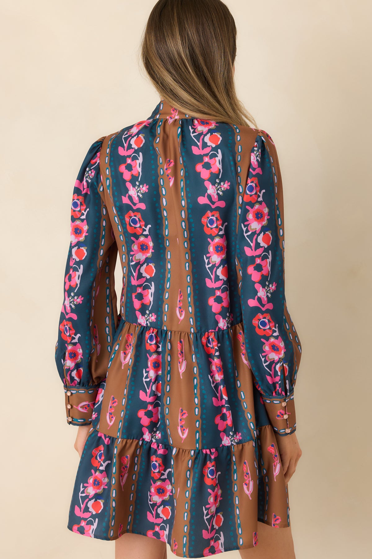 Rear view of the teal and caramel striped floral mini dress with gathered long sleeves and a flowing tiered skirt.