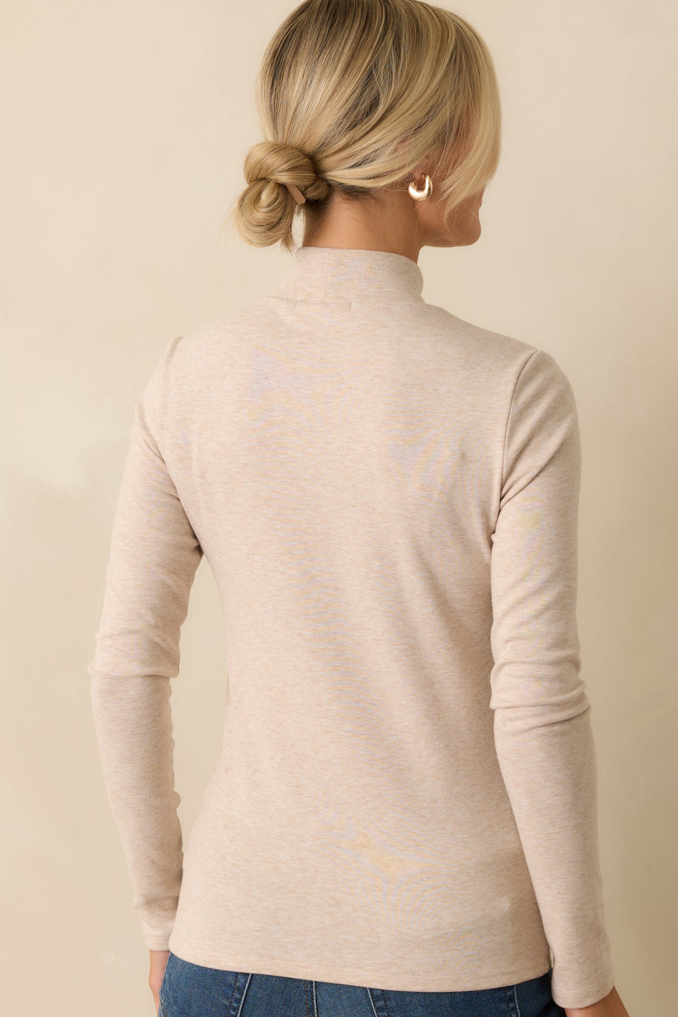 Rear view of the beige long-sleeve top showing slightly fitted silhouette and turtleneck.