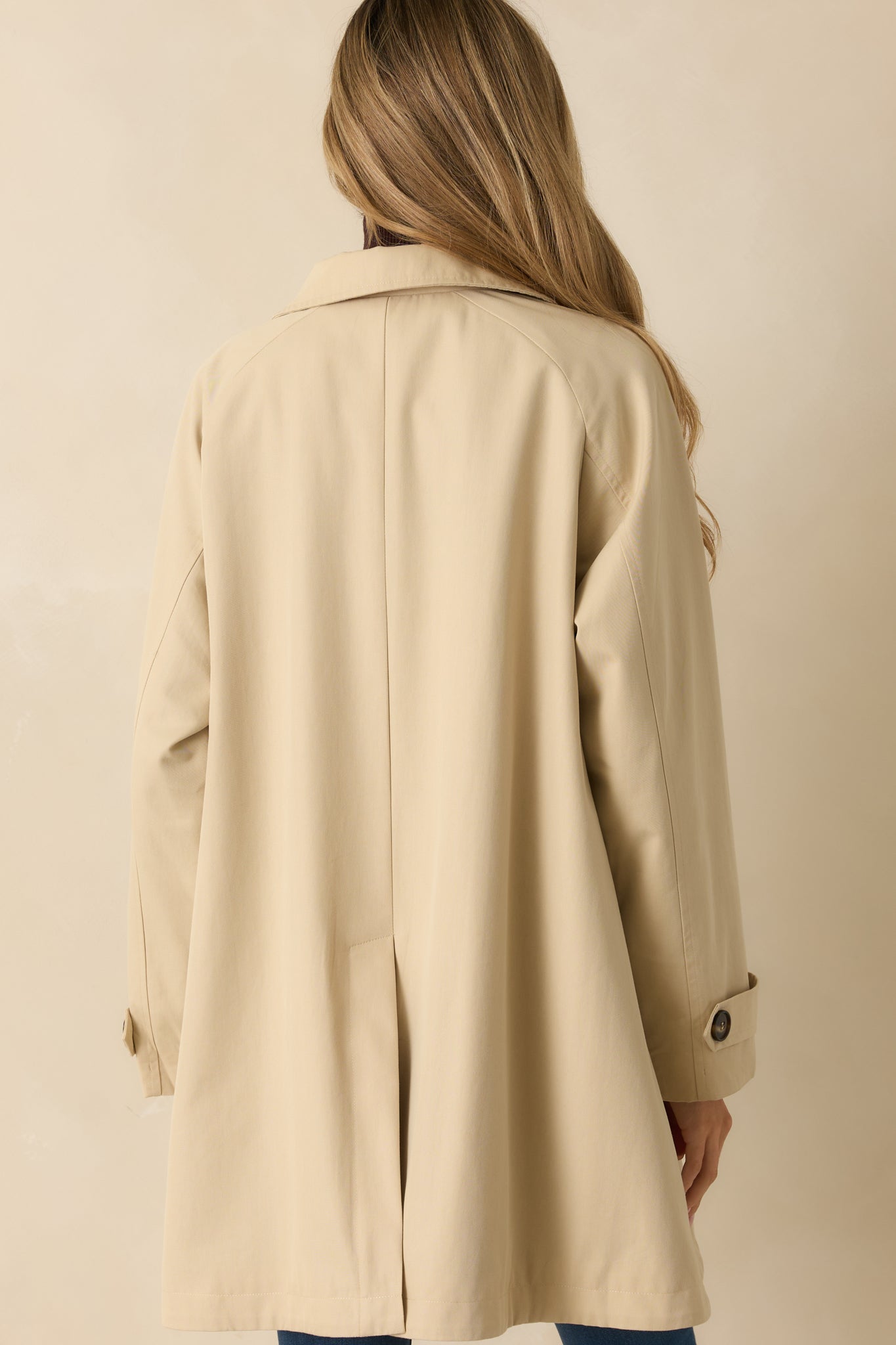 Rear view of beige trench jacket showing long sleeves, clean back silhouette, and structured fit.