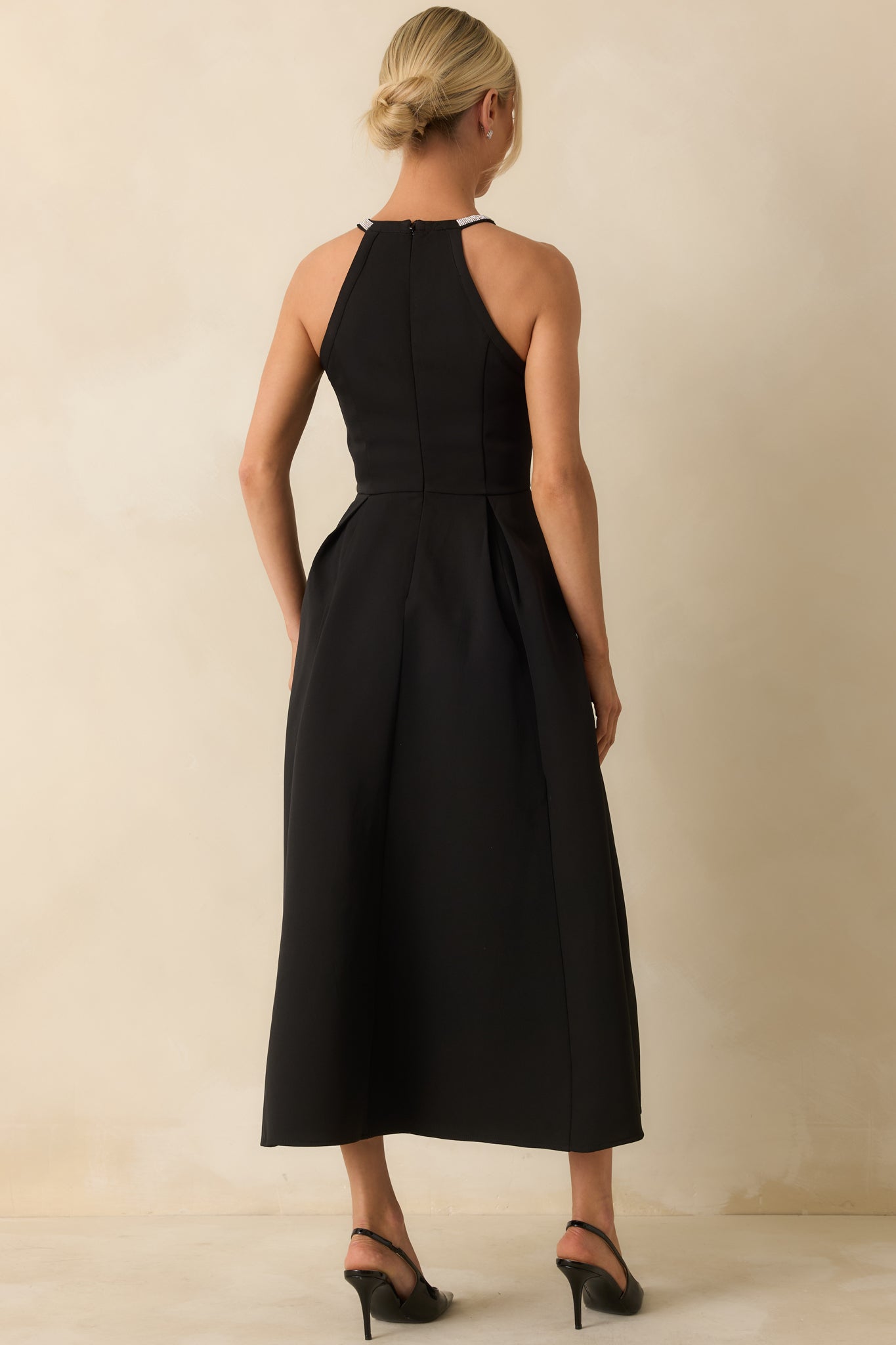 Rear view of the black halter midi dress showing the hidden back zipper and flowy pleated skirt.

