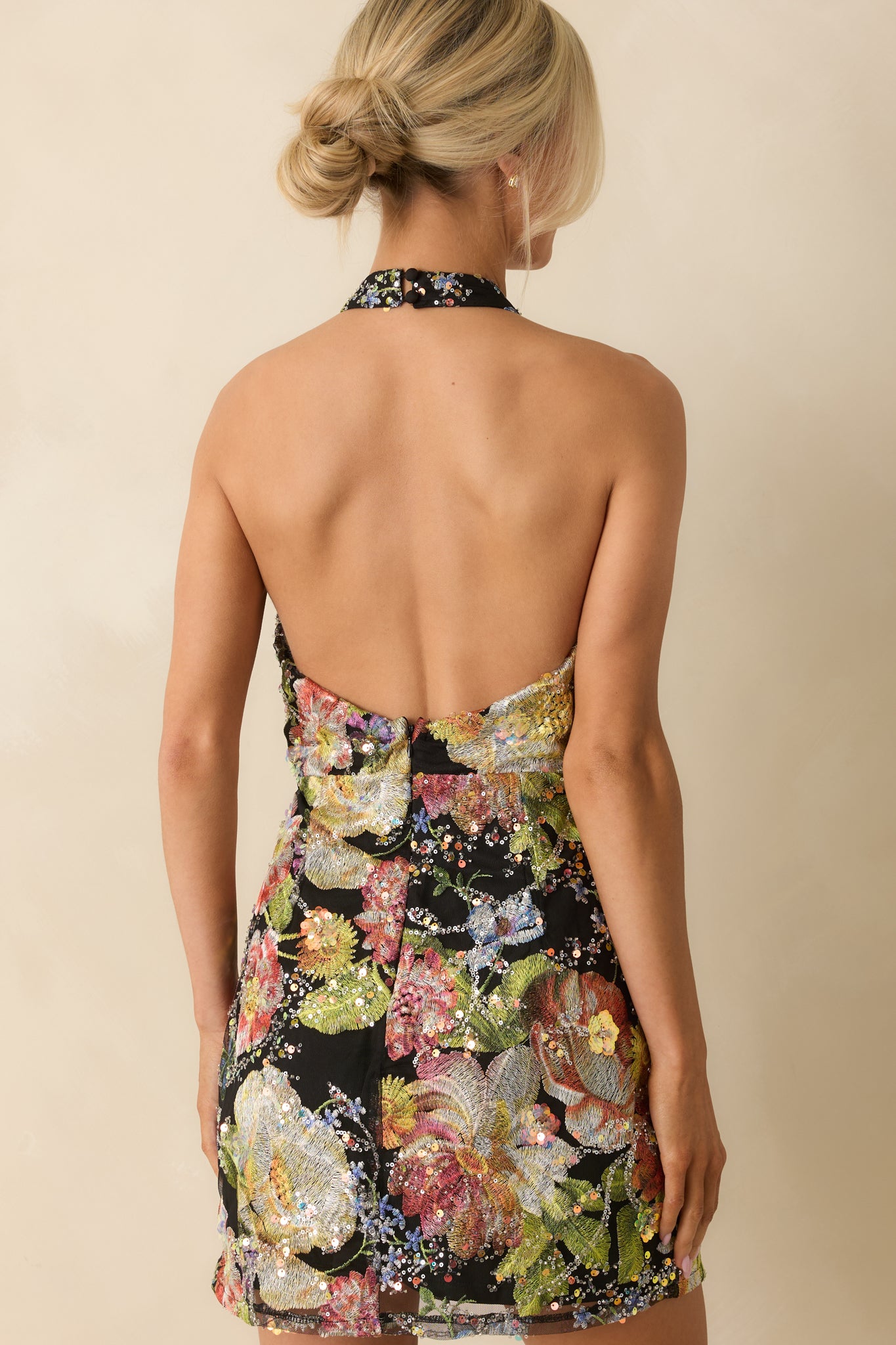 Rear view of black halter mini dress featuring open back and concealed zipper closure.
