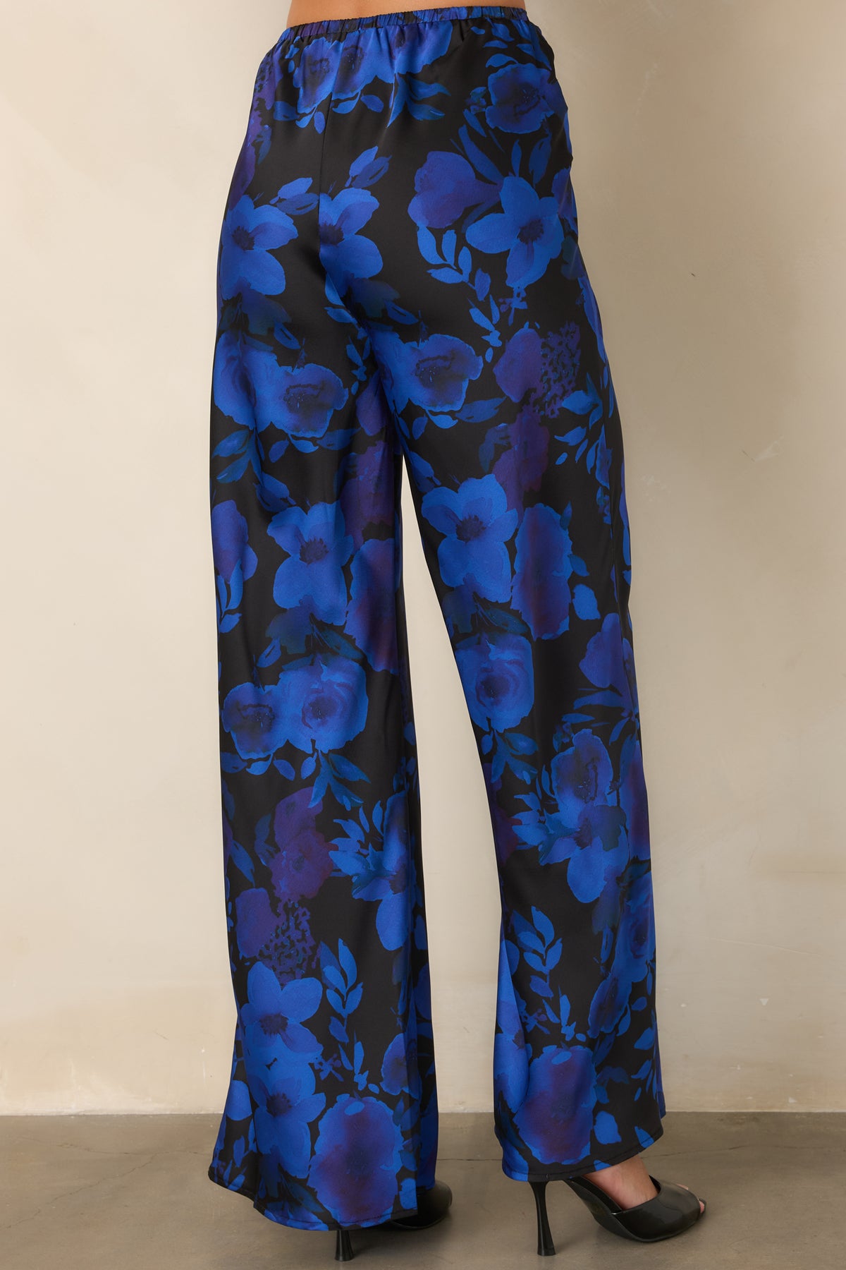 Rear view of the black satin pants showing the elasticized back waistband and flowing wide-leg shape.