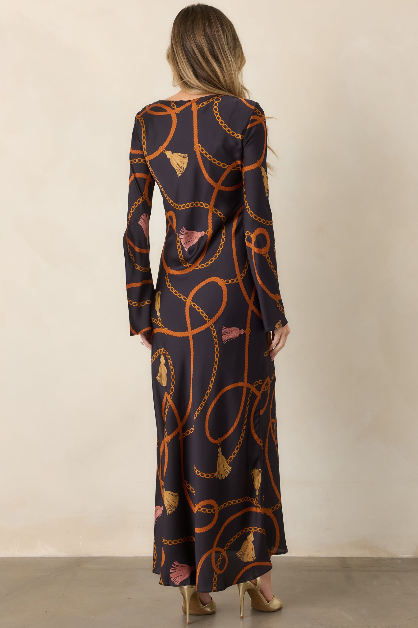 Rear view of the black satin maxi dress showcasing its softly flowing silhouette, long sleeves, and ornate patterned fabric.