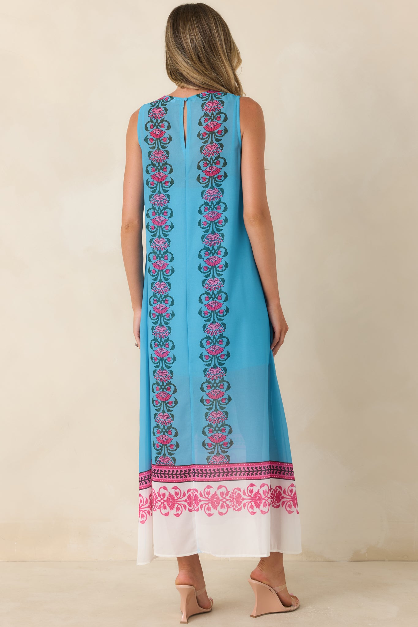Rear view of the blue maxi dress showcasing its flowing silhouette, sleeveless design, and uninterrupted floral border pattern extending to the hem.