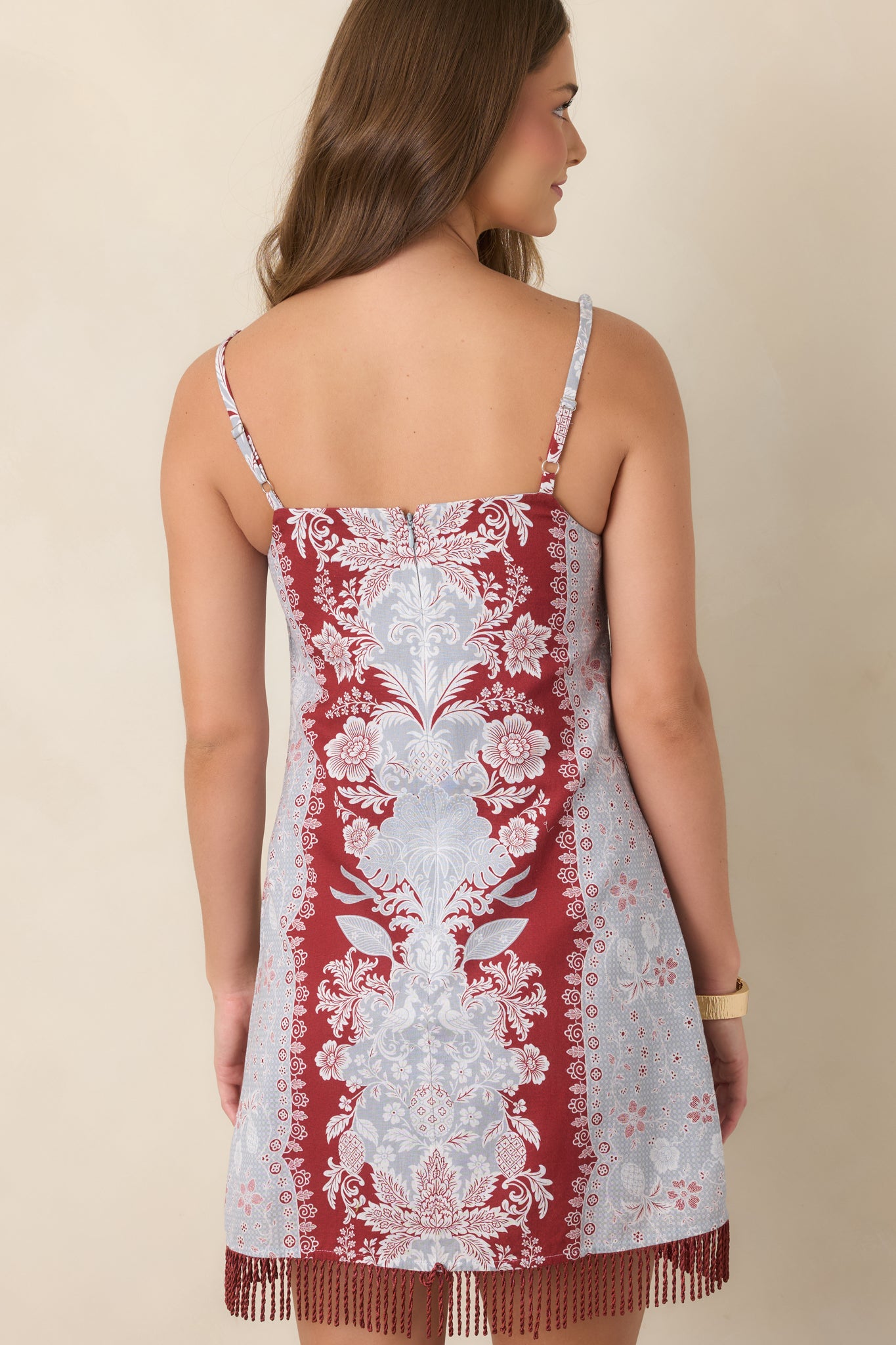 Rear view of the cotton-linen mini dress showing the softly fitted silhouette, concealed zipper, adjustable straps, and fringed hem.
