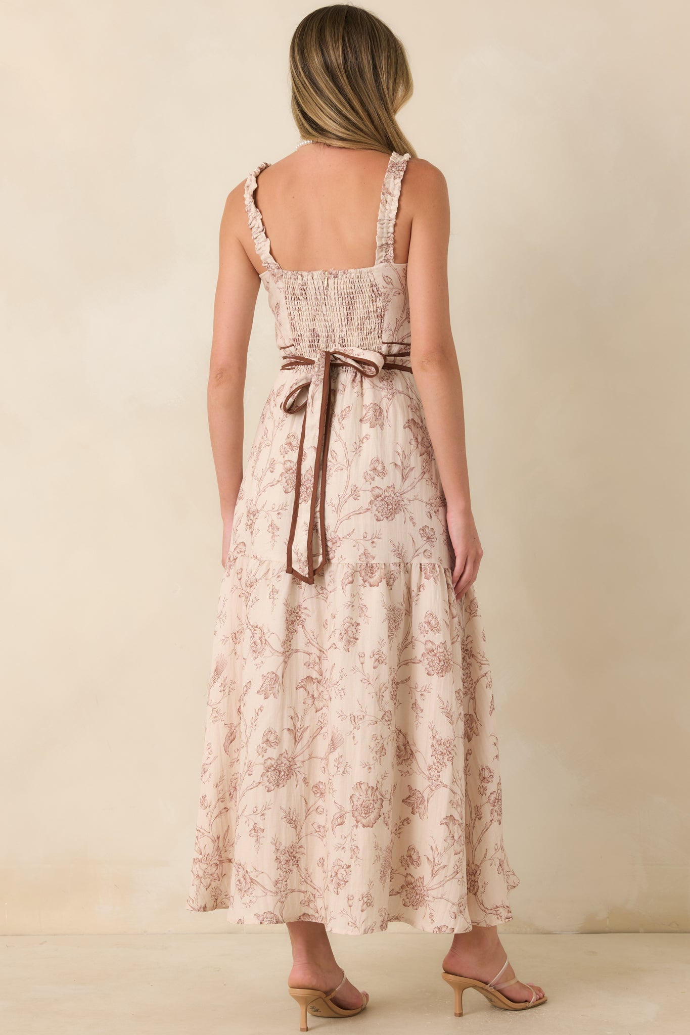 Rear view of the botanical maxi dress highlighting the smocked back, adjustable tie bow, and flowing tiered skirt.