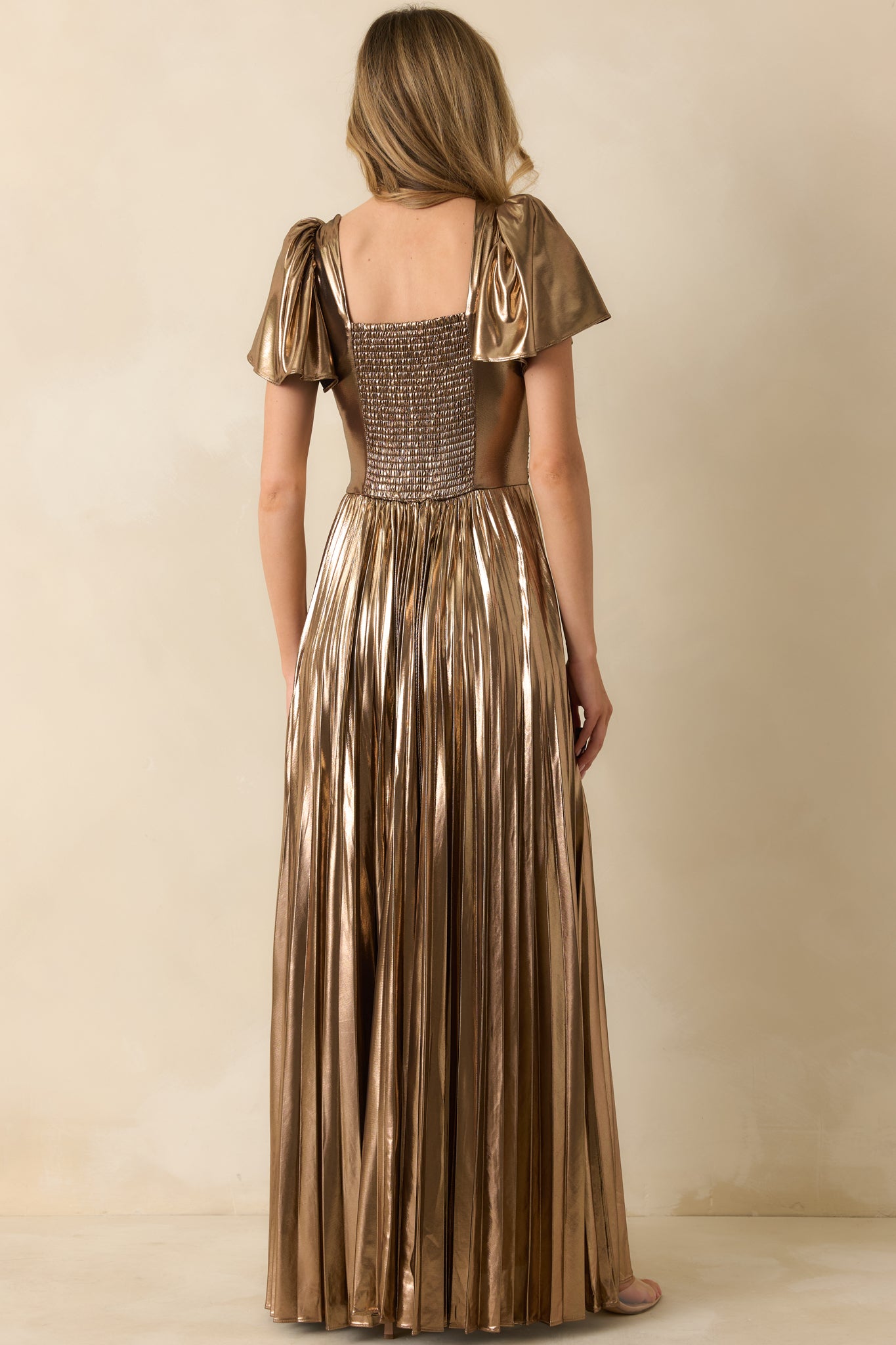 Rear view of the bronze metallic maxi dress showing the smocked back panel and flowing pleated A-line skirt.