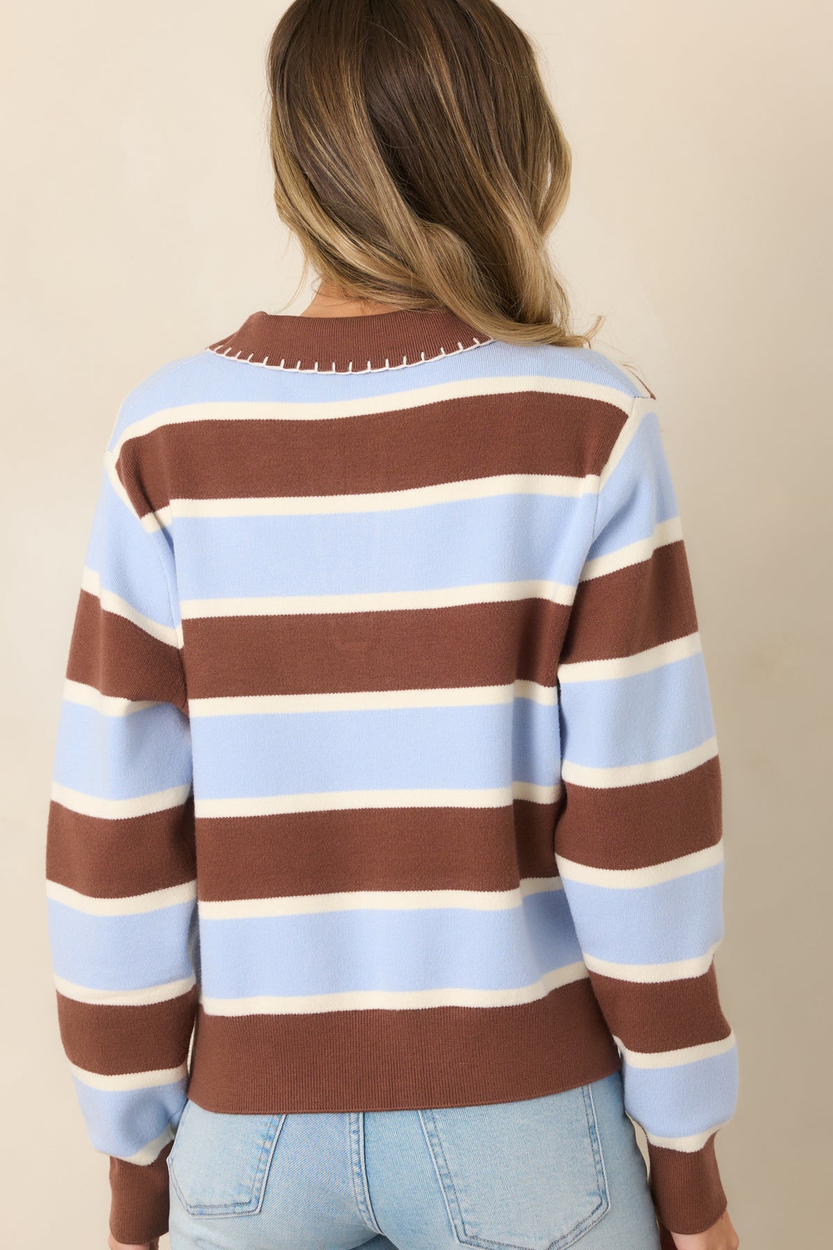 Rear view of the brown, light blue, and white color-blocked knit top showcasing its bold horizontal stripes, relaxed silhouette, long sleeves, and ribbed cuffs.