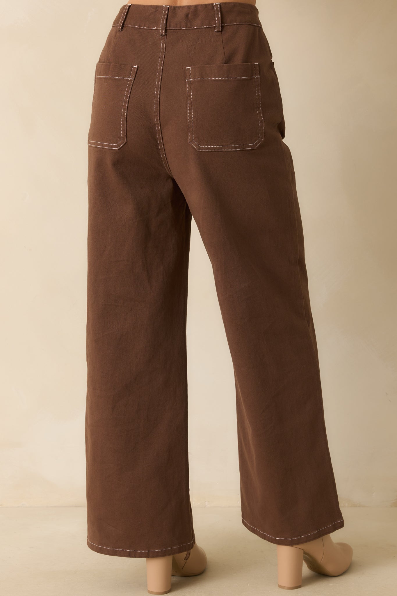 Rear view of brown cotton pants highlighting back patch pockets, wide-leg fit, and topstitching accents.