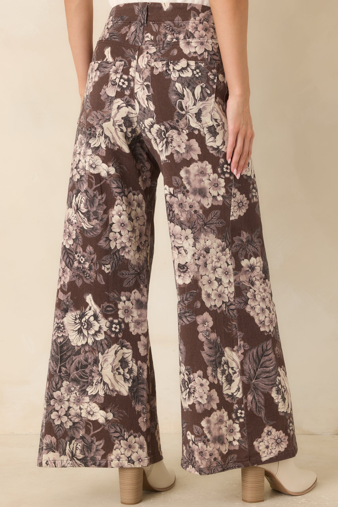 Rear view of the high-rise floral pants showcasing the rich brown background, ivory print, back patch pockets, belt loops, and wide-leg silhouette.