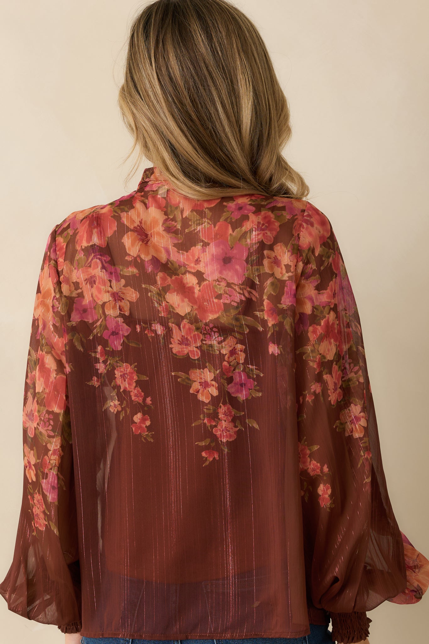 Rear view of brown multi floral blouse showing flowy silhouette, blouson sleeves, and lightweight sheer fabric.