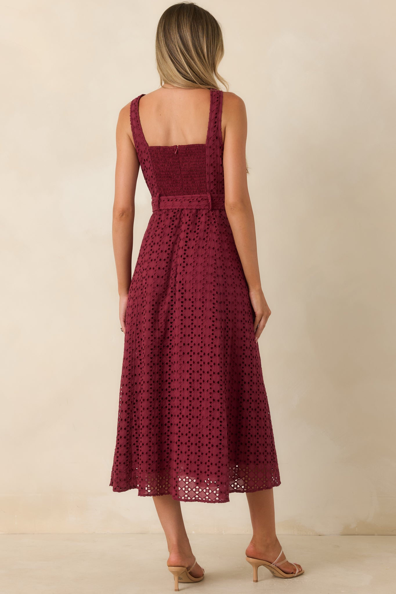Rear view of the burgundy cotton eyelet midi dress featuring a sleeveless silhouette, removable belt, lined design, and embroidered texture.