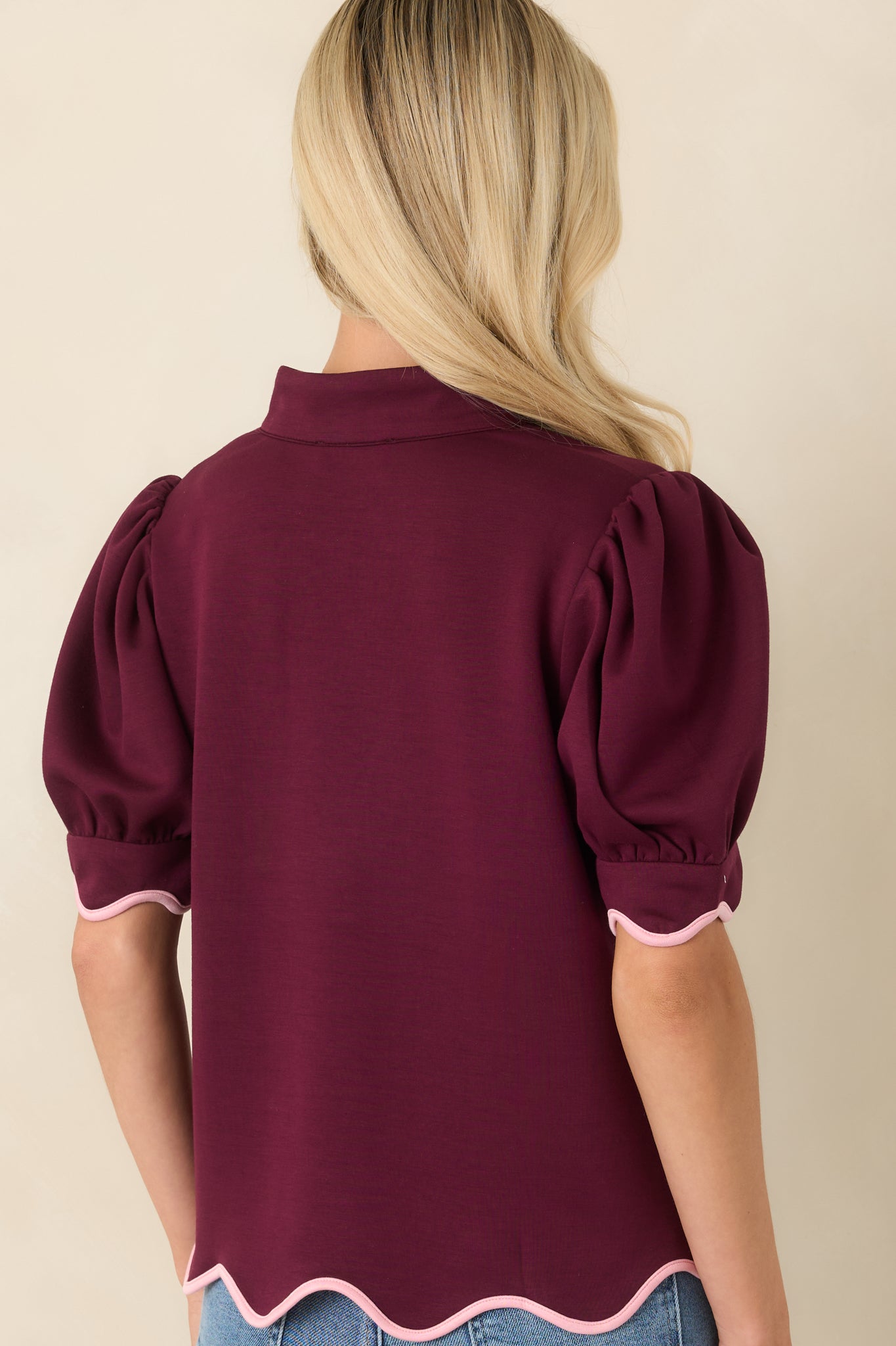 Rear view of the burgundy knit top displaying its relaxed silhouette, puff sleeves, and blush pink trim along the hem.