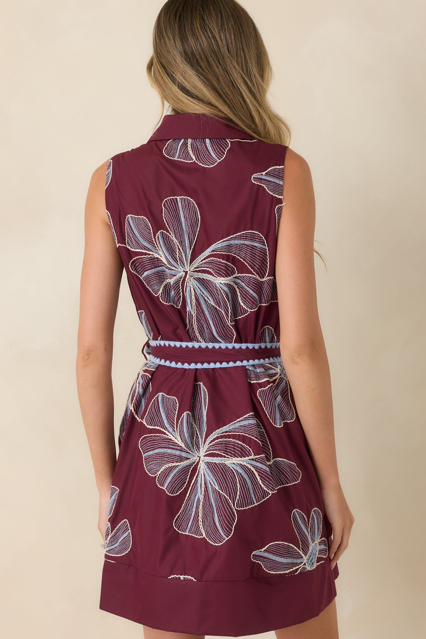 Rear view of the burgundy mini dress showcasing the sleeveless silhouette, softly tailored shape, and embroidered floral details throughout.