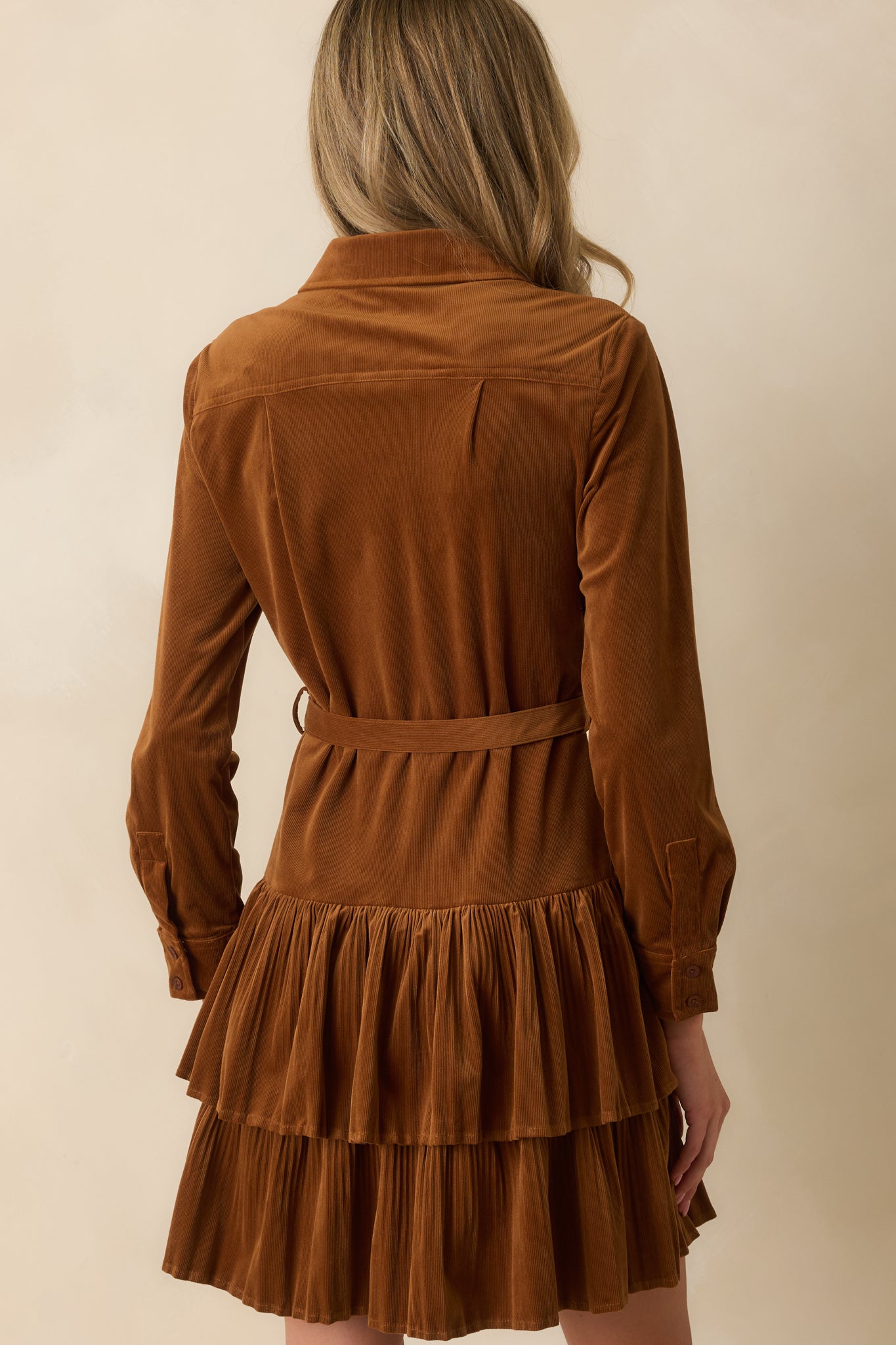 Rear view of caramel brown corduroy mini dress with tiered skirt, long sleeves, and smooth back silhouette.