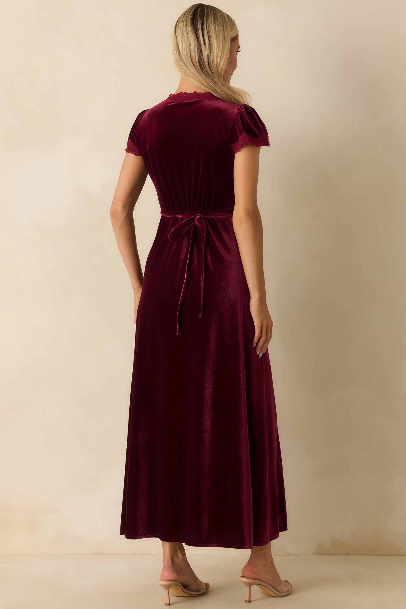 Rear view of cranberry red velvet maxi dress showing flutter sleeves, empire waist, and flowing A-line skirt.