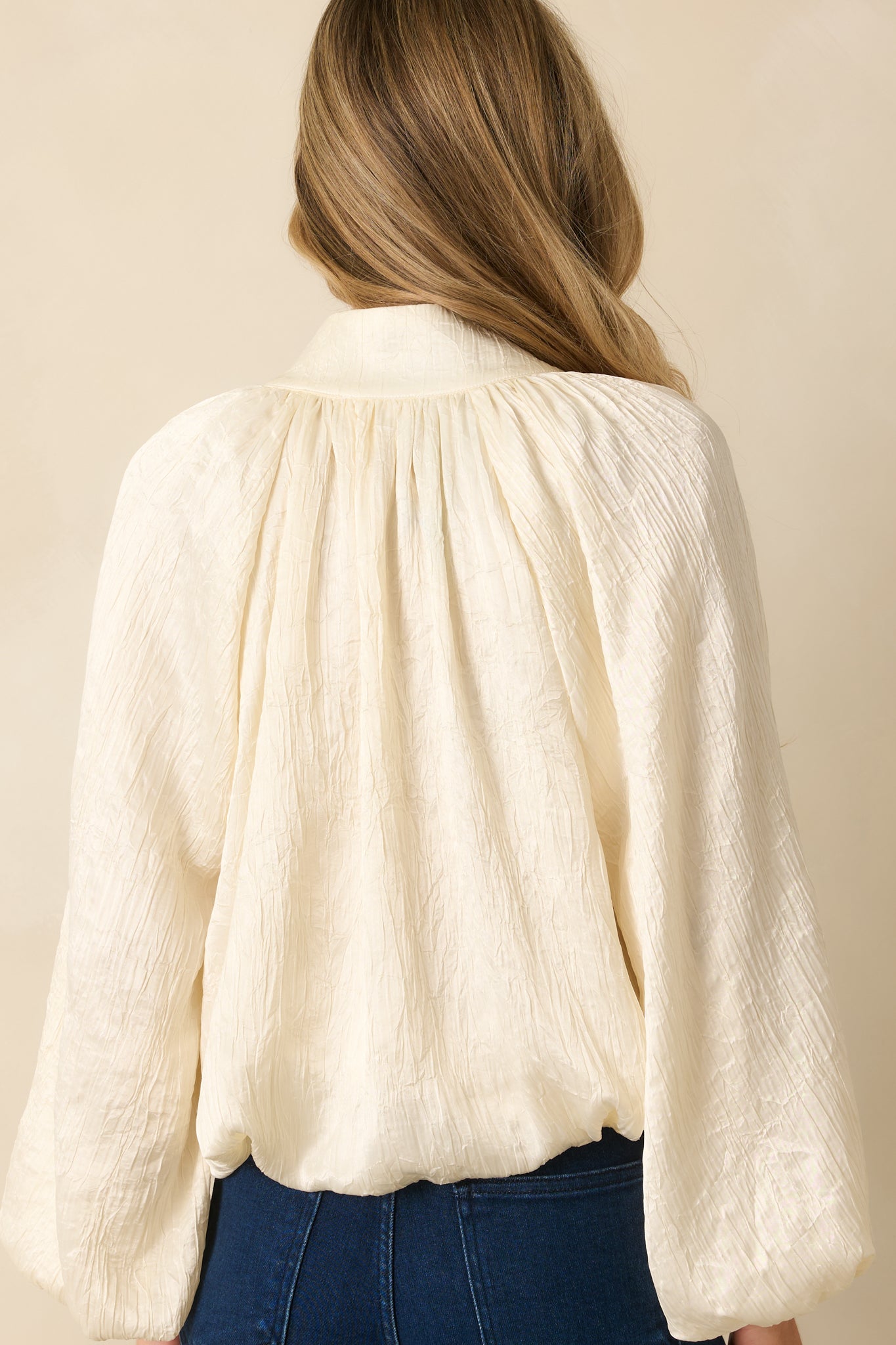 Rear view of the cream satin V-neck top highlighting the relaxed silhouette and long peasant sleeves.