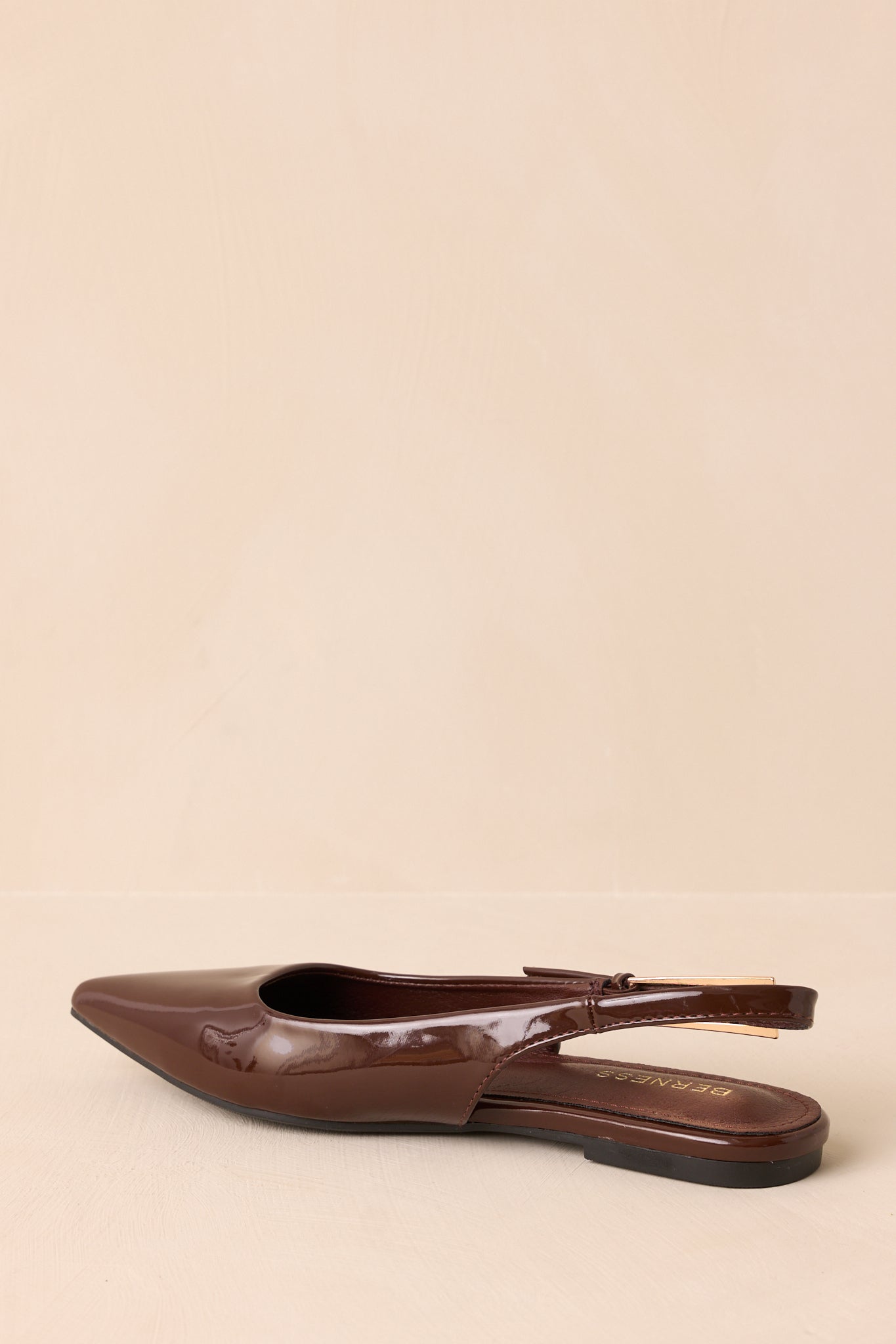 Rear view of dark brown patent flats displaying the slingback strap and polished finish.