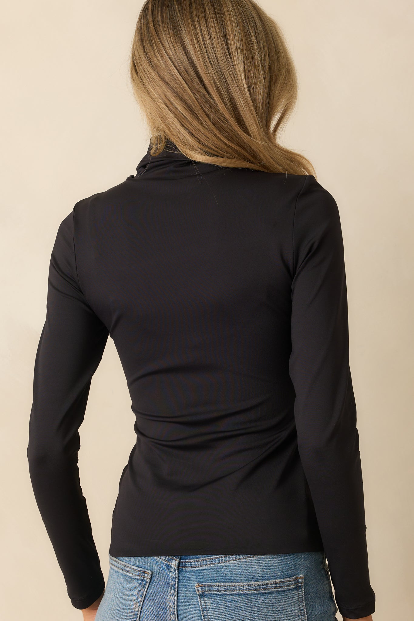 Rear view of the black turtleneck top displaying the smooth fabric and contoured fit.