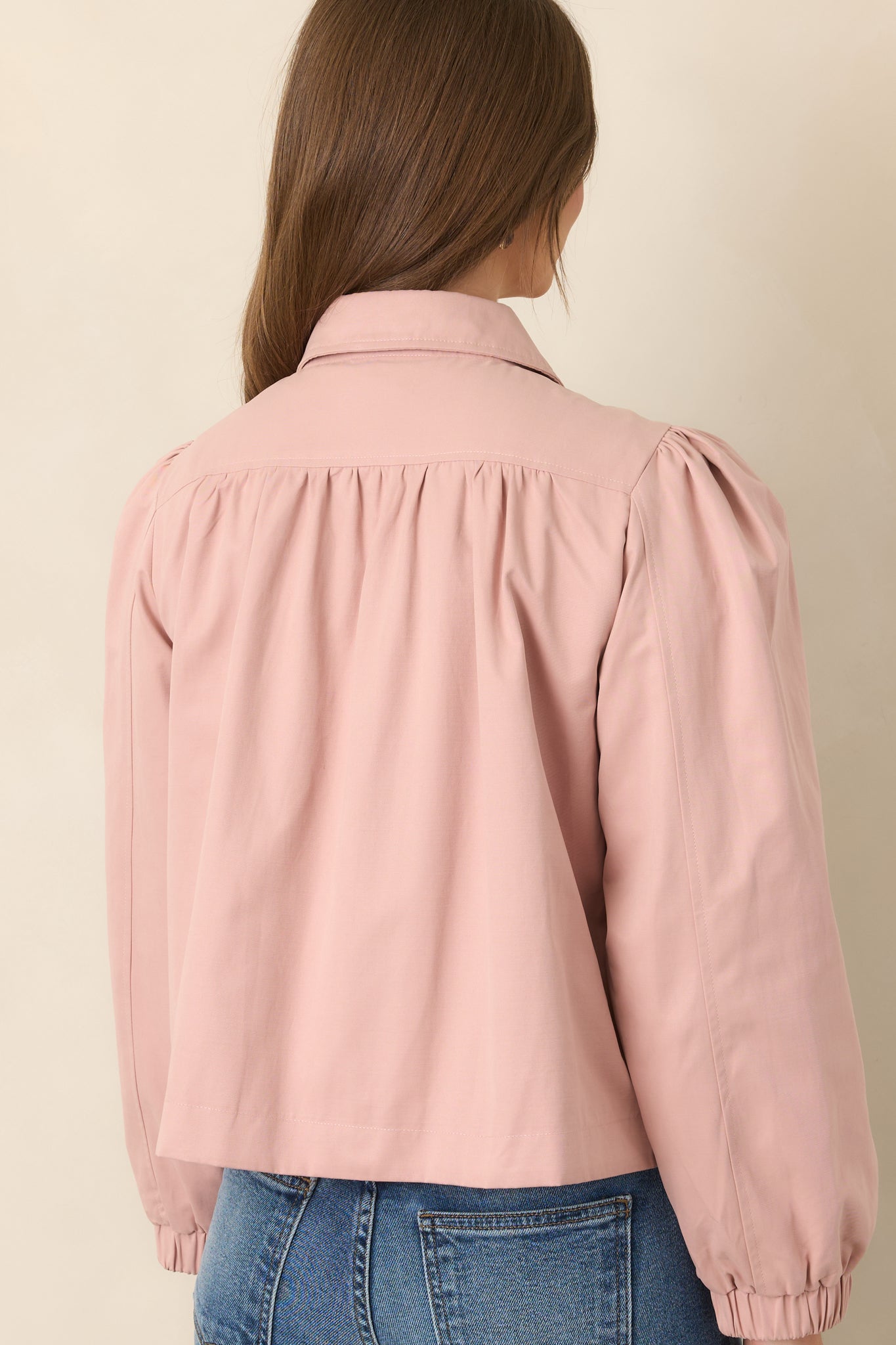 Rear view of the dusty pink cropped jacket showcasing the gathered shoulders, softly rounded puff sleeves, elasticized cuffs, and relaxed silhouette.