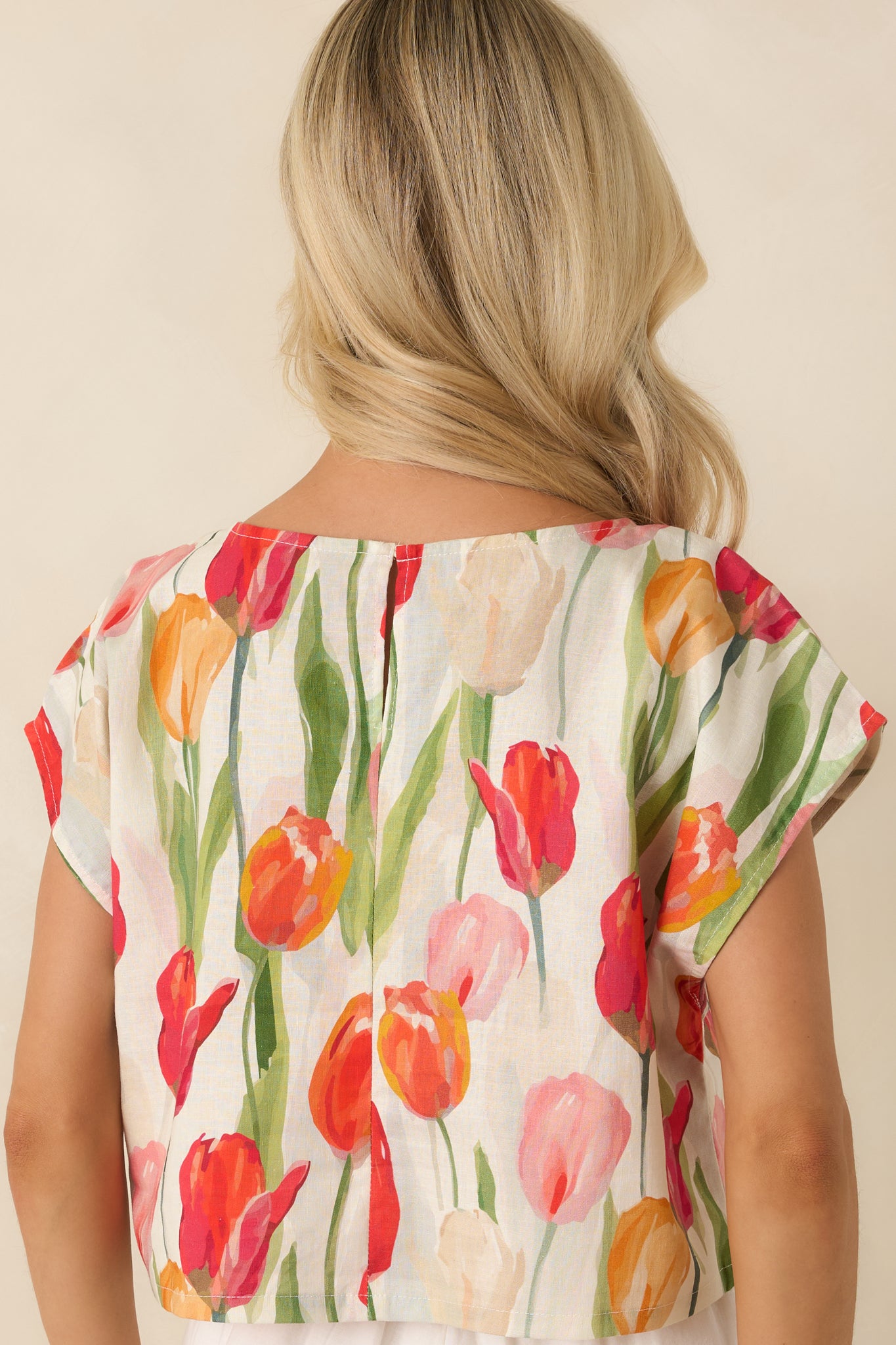 Rear view of the ivory multi floral cropped top featuring cap-style sleeves, a relaxed silhouette, and lightweight linen blend fabric.