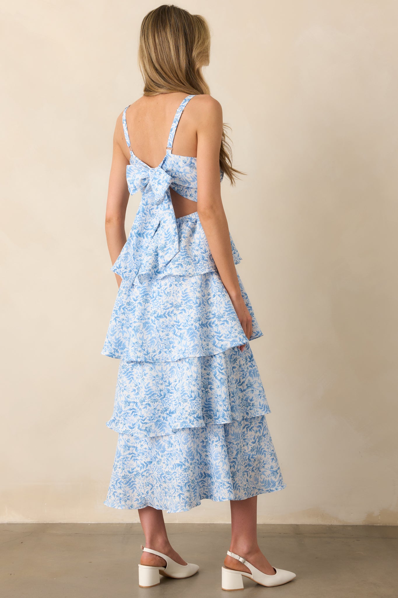 A rear view of the blue floral maxi dress, featuring an open back design with a self-tie bow and an elastic back waist insert. The tiered skirt flows from the back for a soft, feminine look.