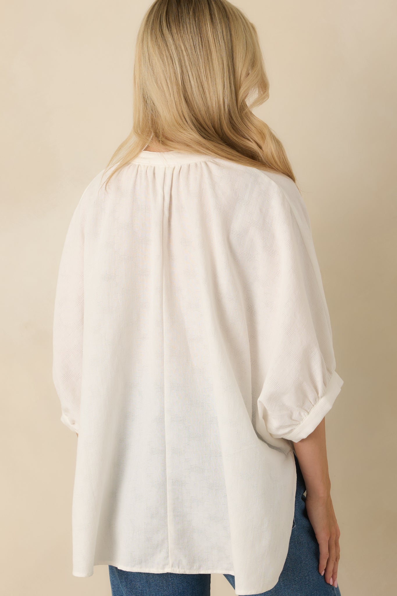 Rear view of blouse featuring gentle back pleating, relaxed silhouette, and softly gathered 3/4 sleeves with elastic cuffs.