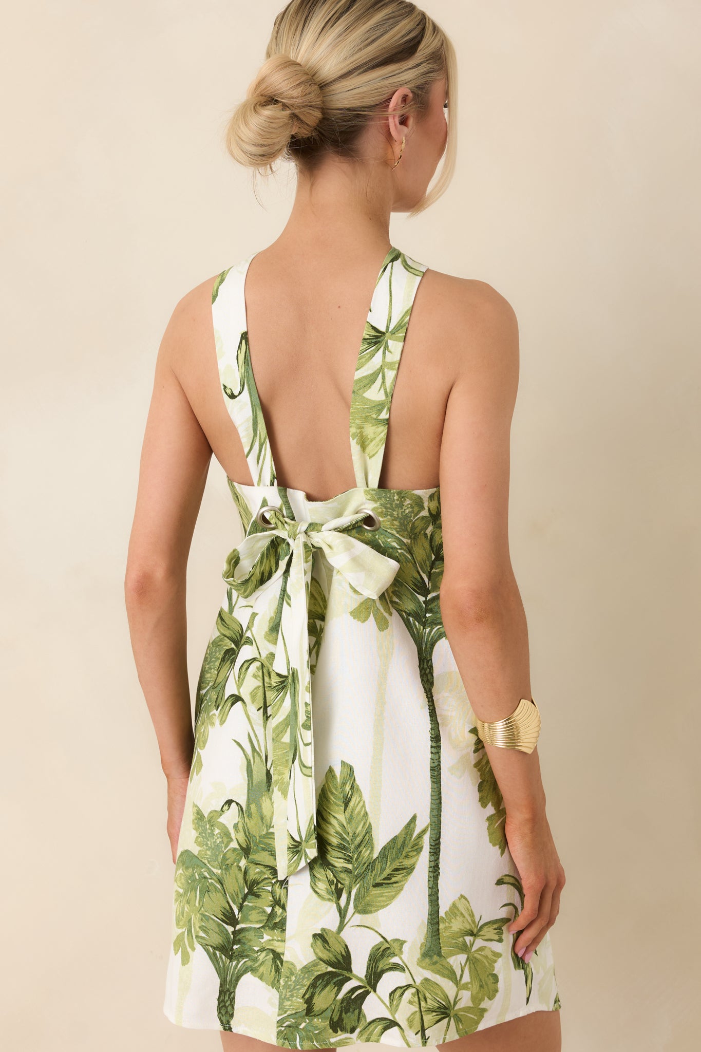 Rear view of ivory and green mini dress featuring open back design with adjustable grommet detailing and functional self-tie bow closure.