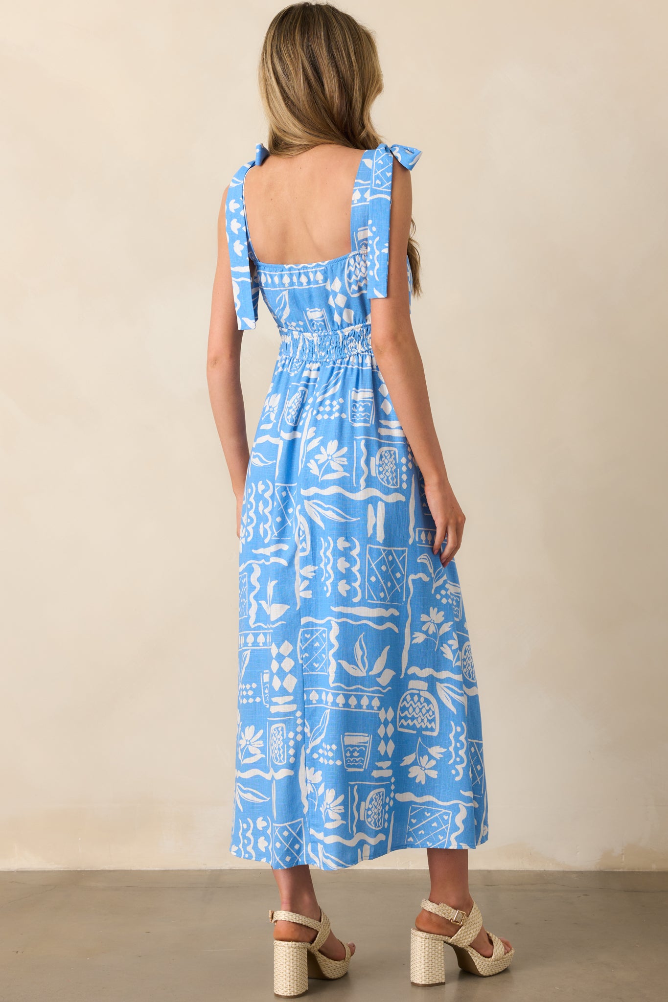 Rear view of blue maxi dress featuring smocked back insert, adjustable shoulder ties, and continued tropical print.