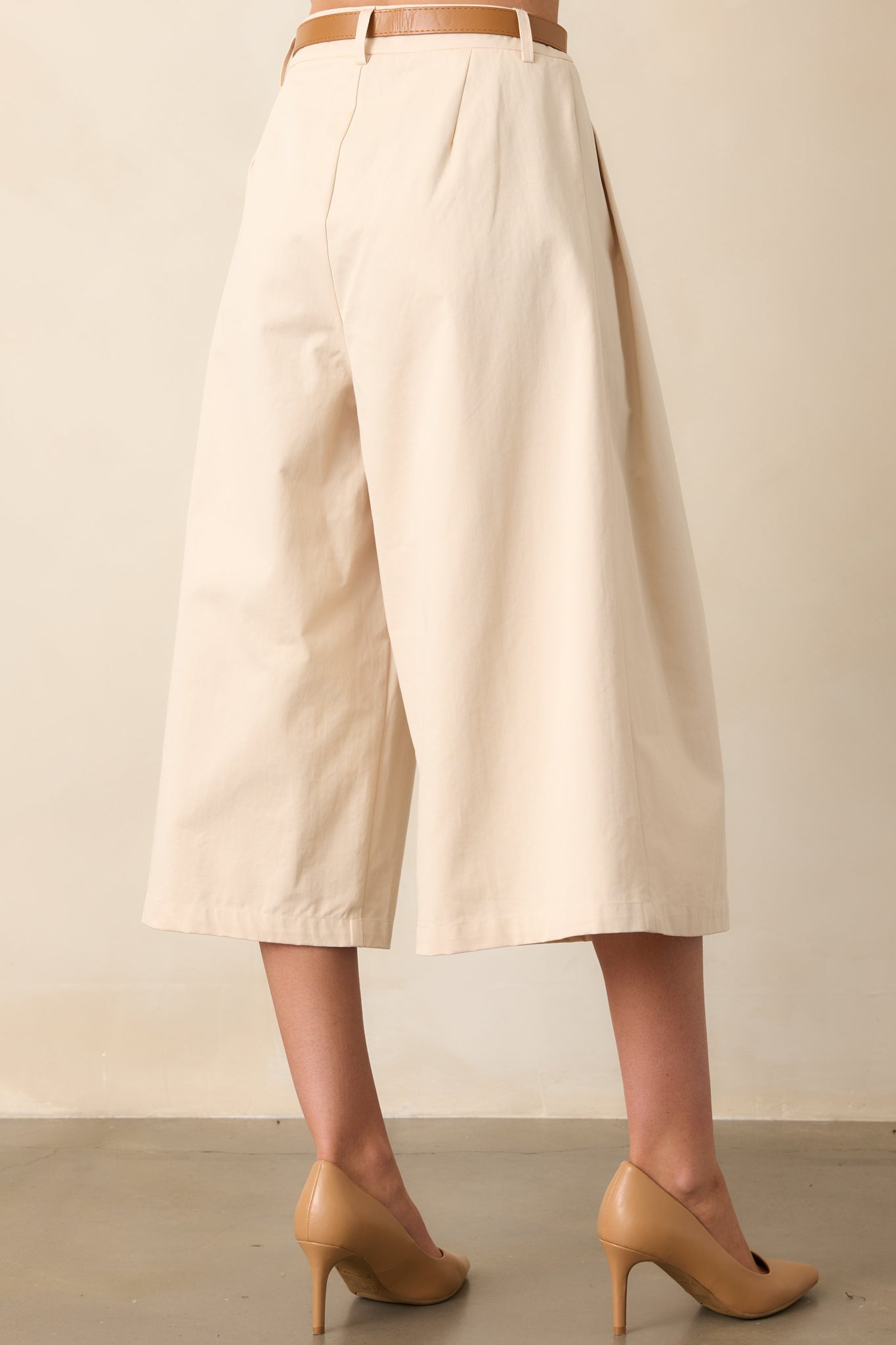 The rear view of beige wide-leg pants, featuring structured pleats and a coordinating belt.
