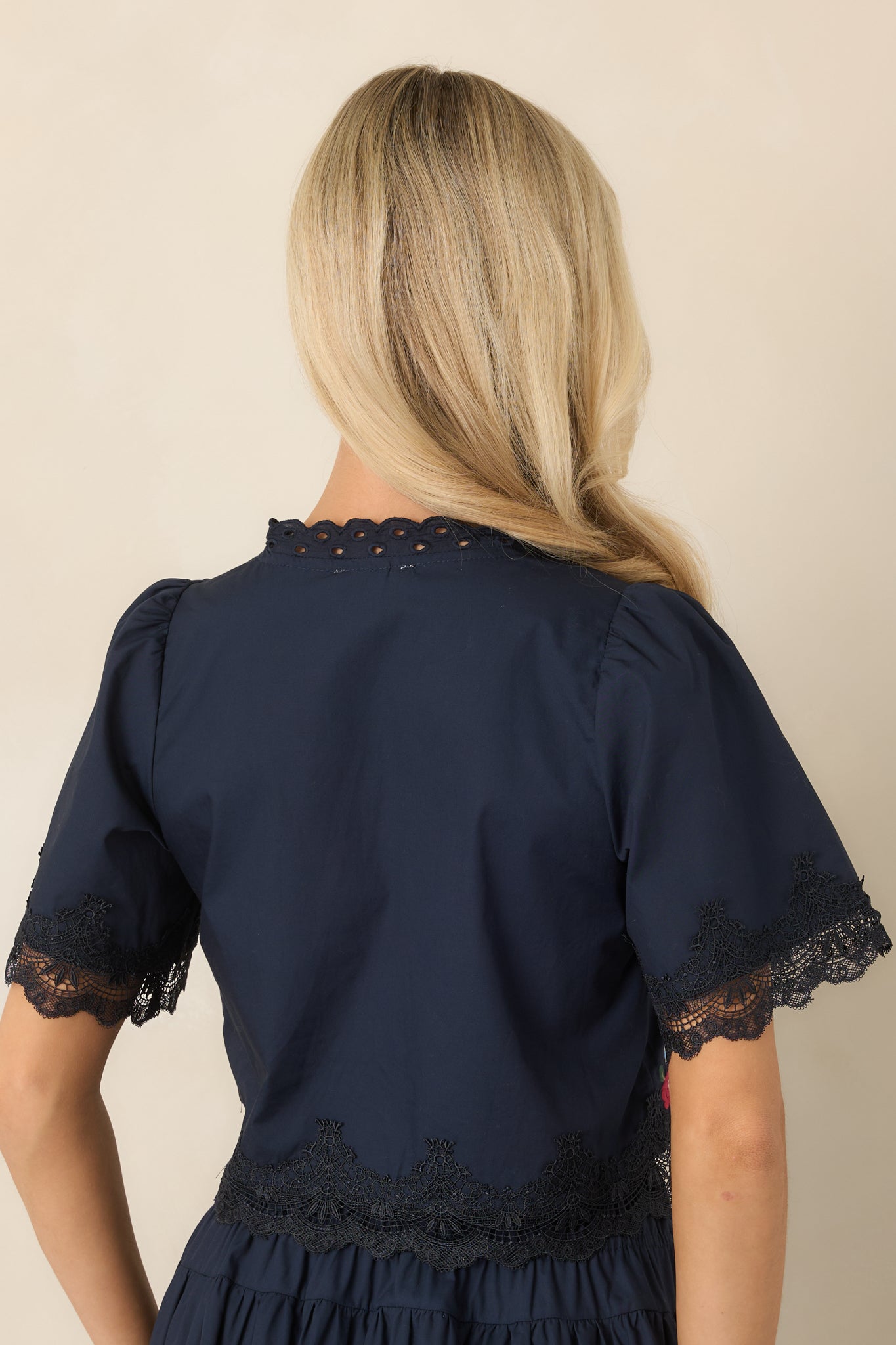 Rear view of the cotton top showcasing its embroidered floral detailing, softly gathered shoulders, short puff sleeves, and lace-trimmed hem.