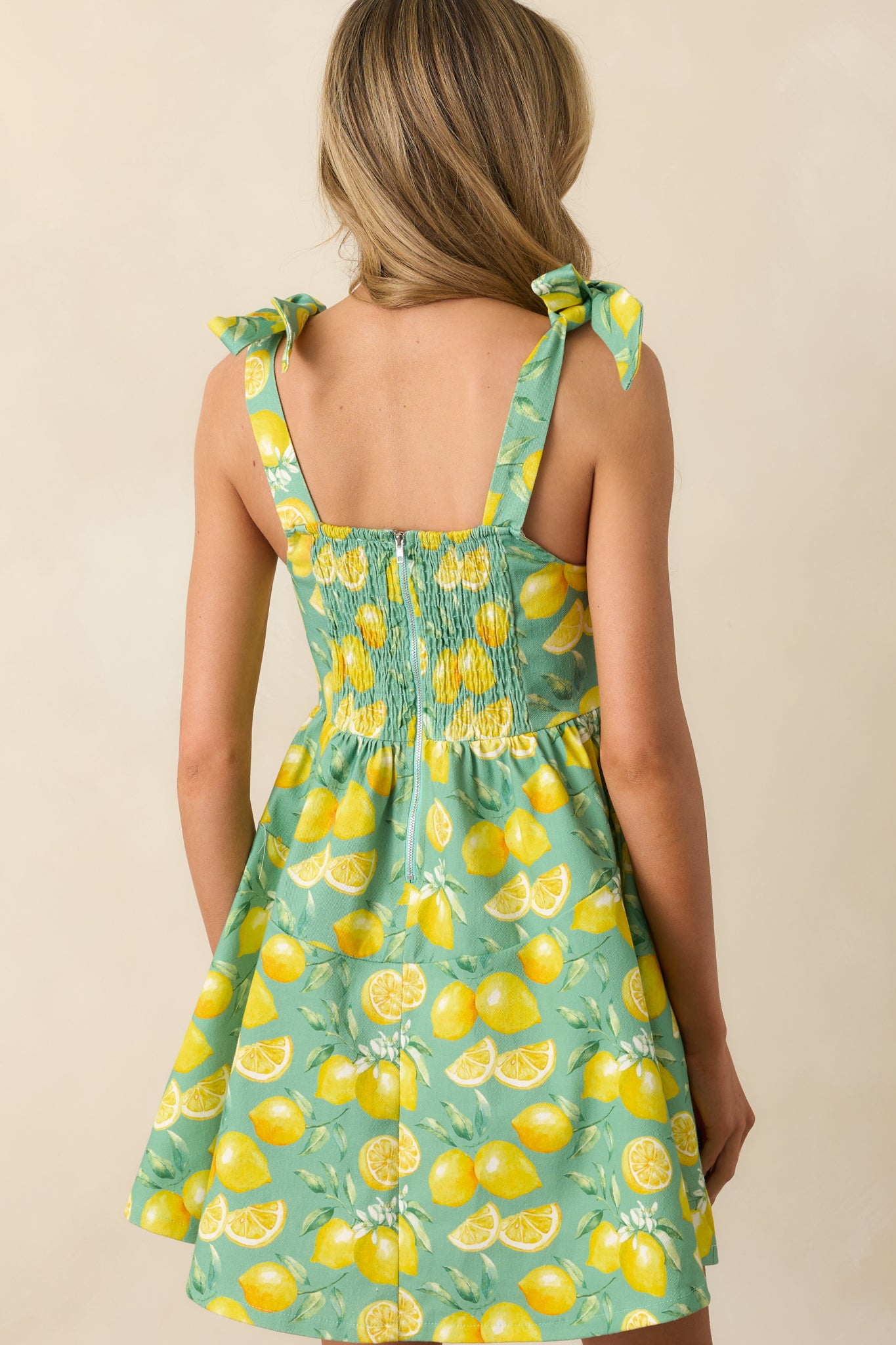 A view from behind of the green mini dress, showing the smocked panel, adjustable straps, and zipper closure.