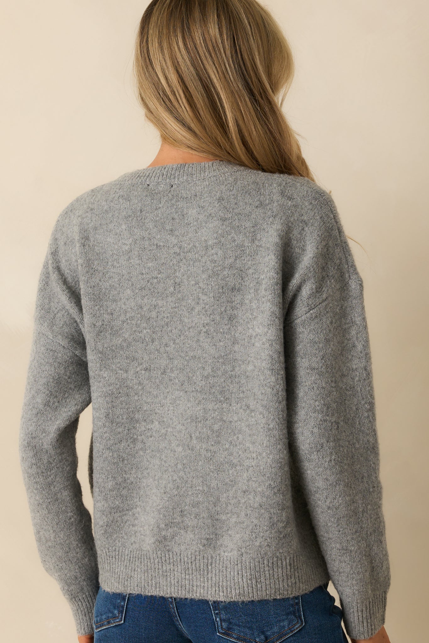 Rear view of grey sweater showing smooth knit fabric and ribbed hem.