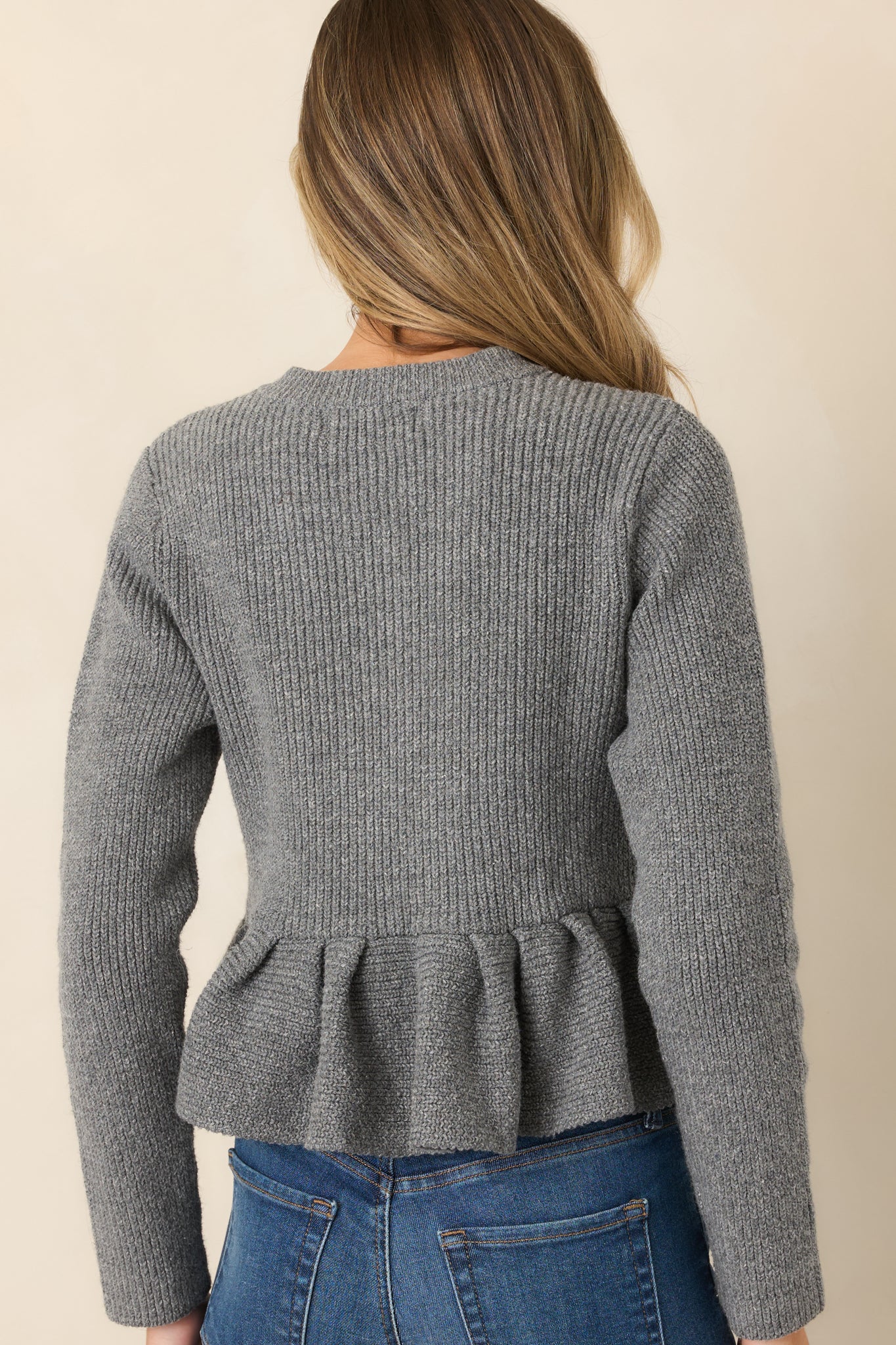 Rear view of the heather gray knit cardigan showcasing its fitted bodice, structured peplum hem, long sleeves, and smooth cotton-blend construction.