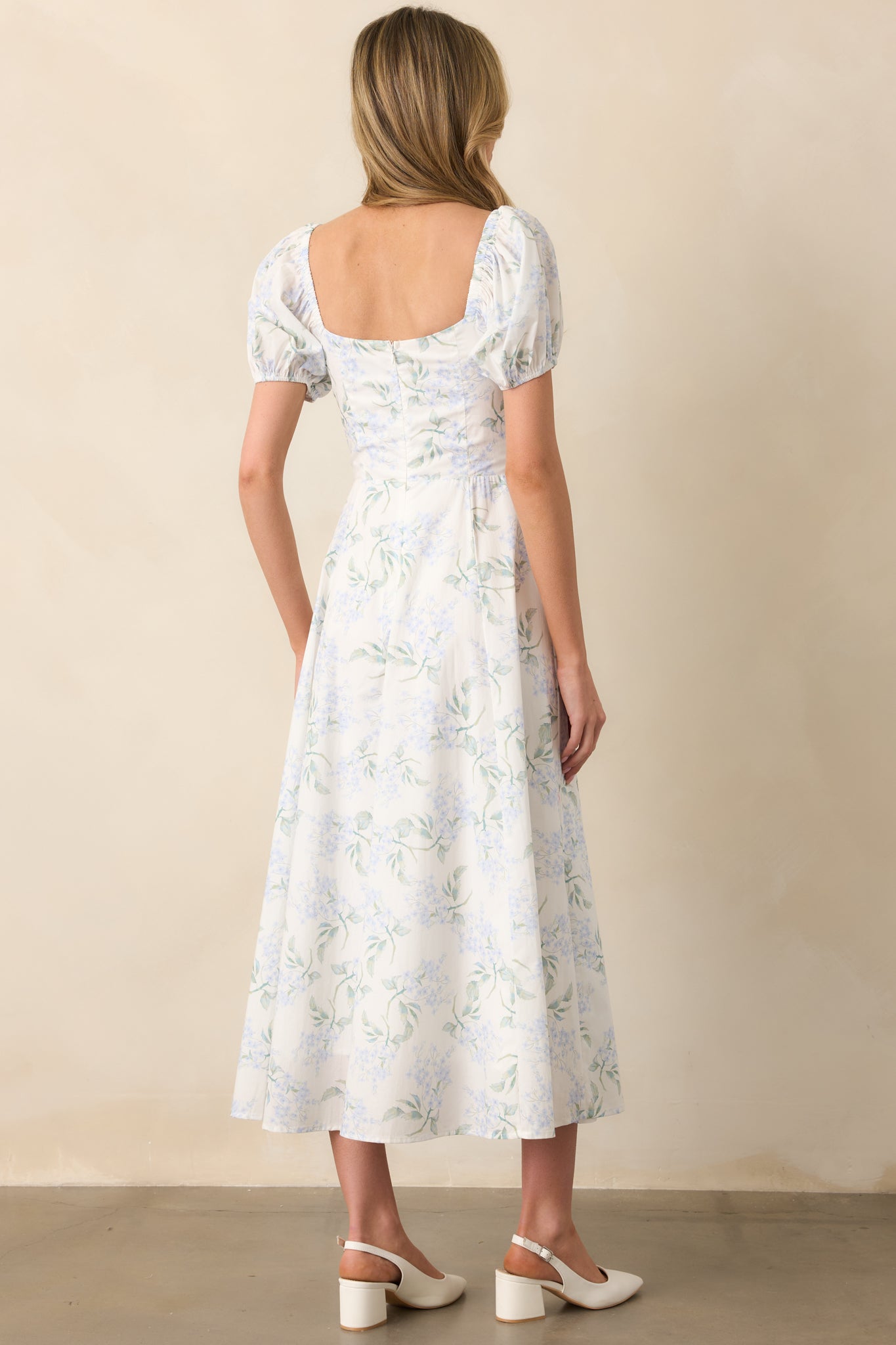 A rear view of the light blue floral print maxi dress, highlighting the hidden back zipper and elastic shoulder straps, along with the puff sleeves and elastic cuffs that complement the dress’s design.