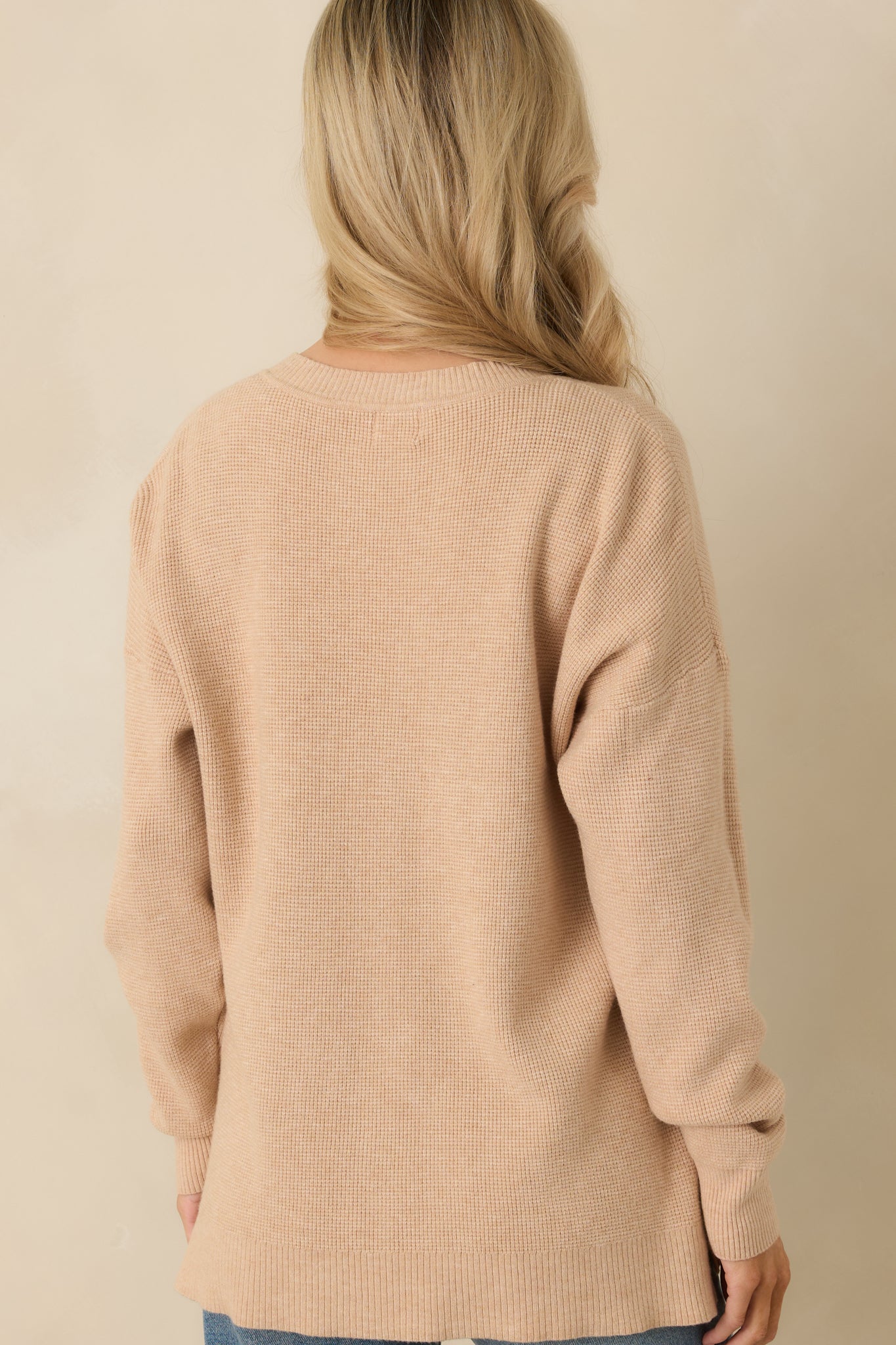 Rear view of light taupe sweater highlighting relaxed fit, long sleeves, and split hem bottom.