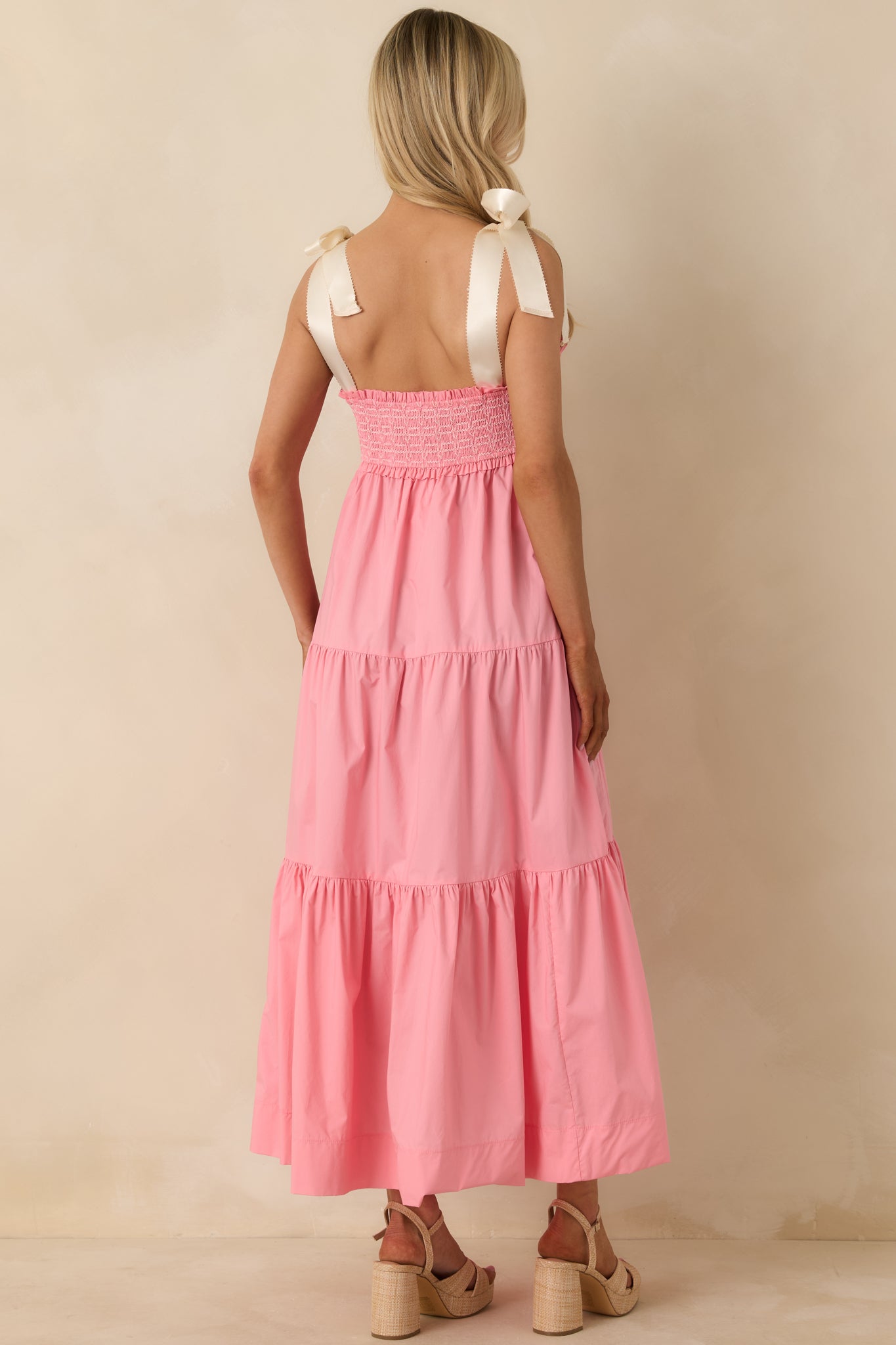 Rear view of pink coral midi dress highlighting smocked back, bow straps, and flowing midi-length hem.