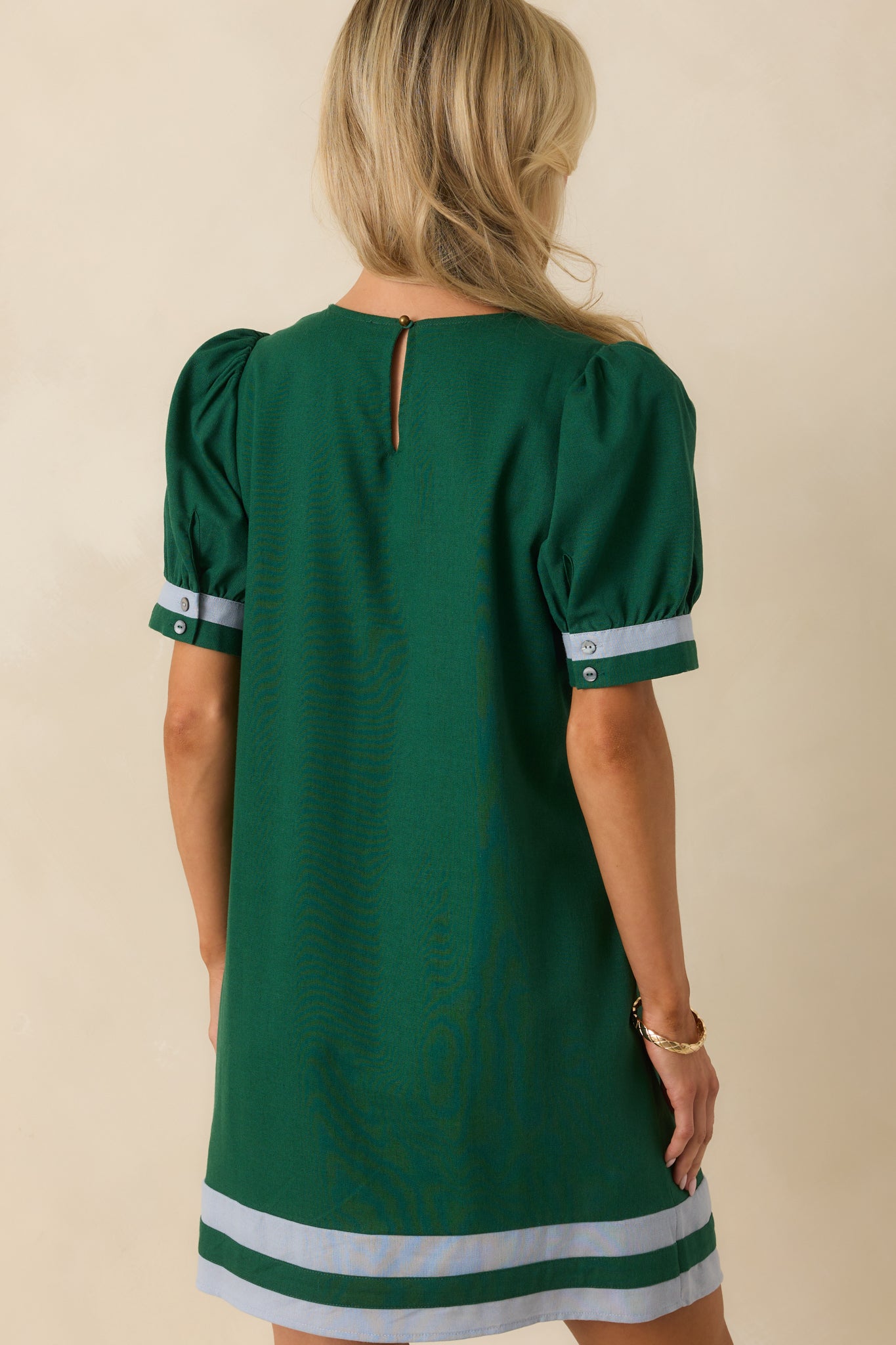Rear view of hunter green mini dress showing back keyhole button closure, short puff sleeves, and functional pockets.