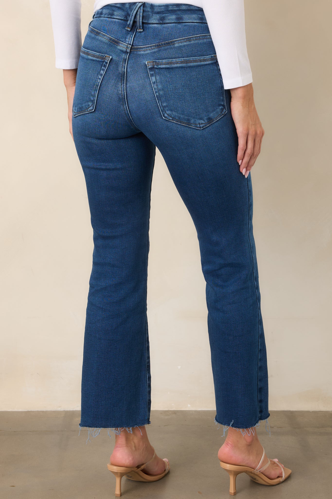 Rear view of the medium indigo jeans showcasing the high-rise waist, slim fit through the hips and thighs, cropped bootcut legs, and raw hems.