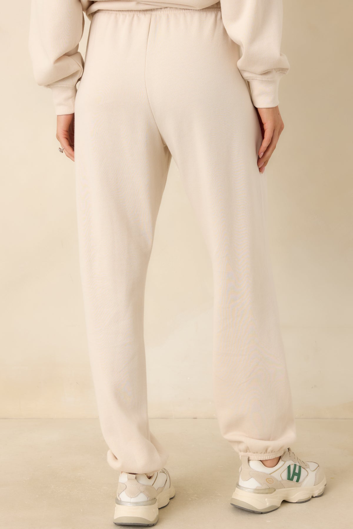 Rear of the warm ivory-beige joggers, showing the relaxed leg shape and gathered ankle cuffs.