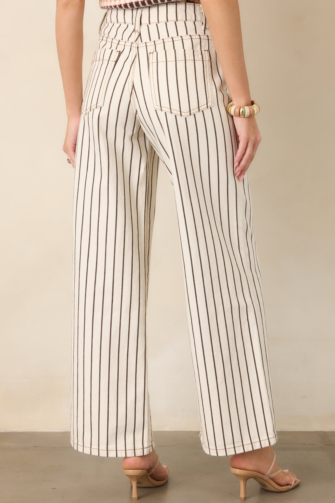 Rear view of the ivory cotton denim pants featuring vertical brown pinstripes, a high-rise waist, back pockets, and relaxed wide legs.