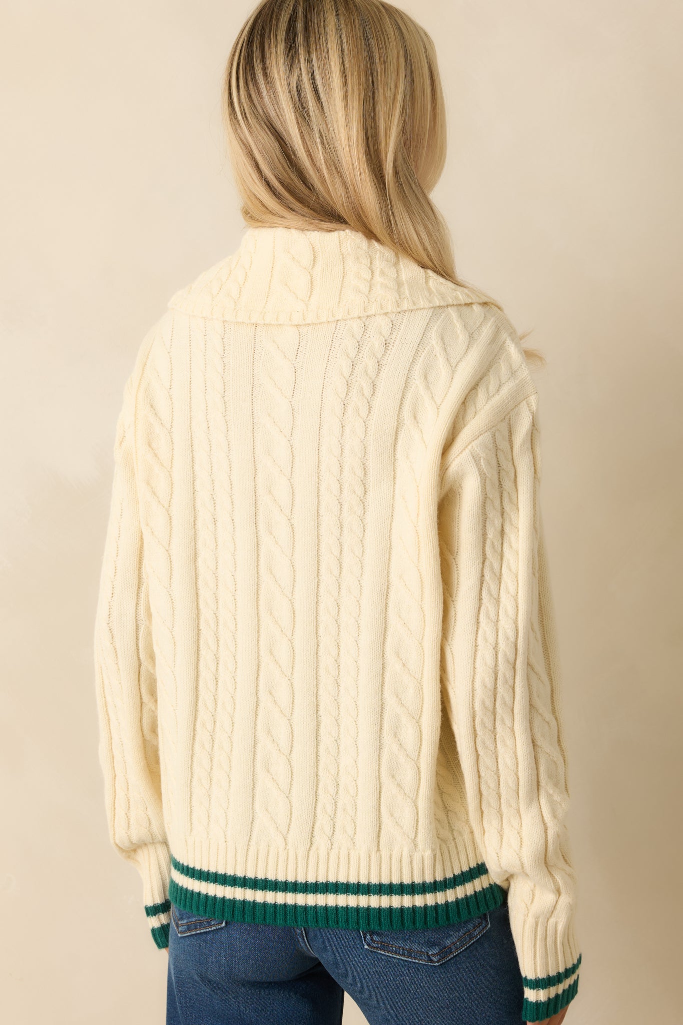 Rear view of ivory cable knit sweater, showing long sleeves, ribbed hem and cuffs, and collared neckline.