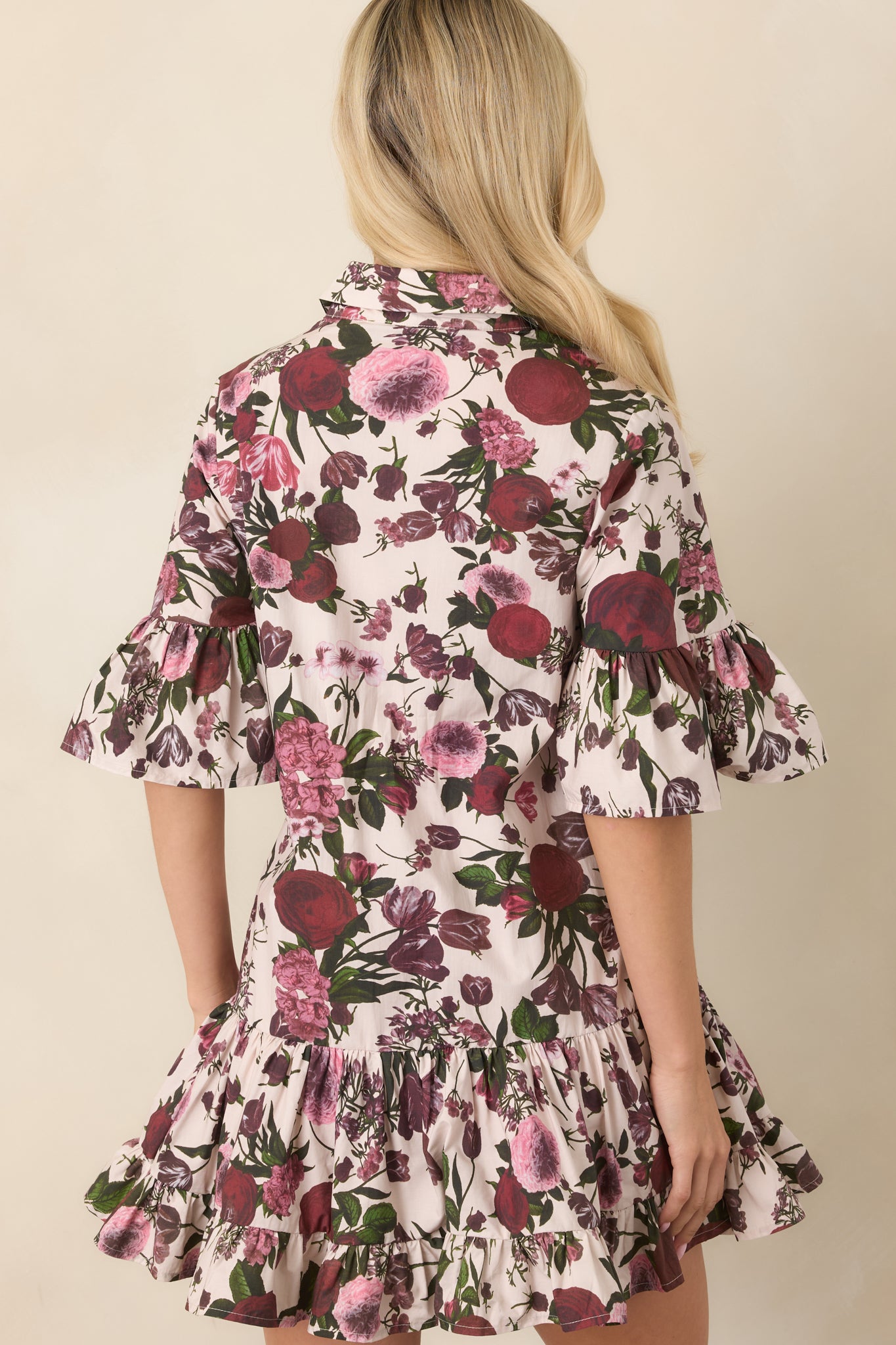 Rear view of the ivory floral cotton mini dress showcasing its ruffled bell sleeves, tiered drop-waist skirt, and colorful botanical print.