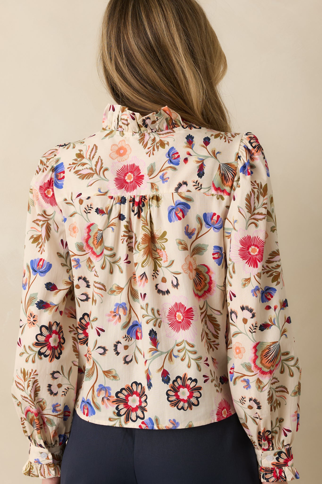 Rear view of ivory floral top showing smooth woven fabric, puff sleeves, and ruffled cuffs.