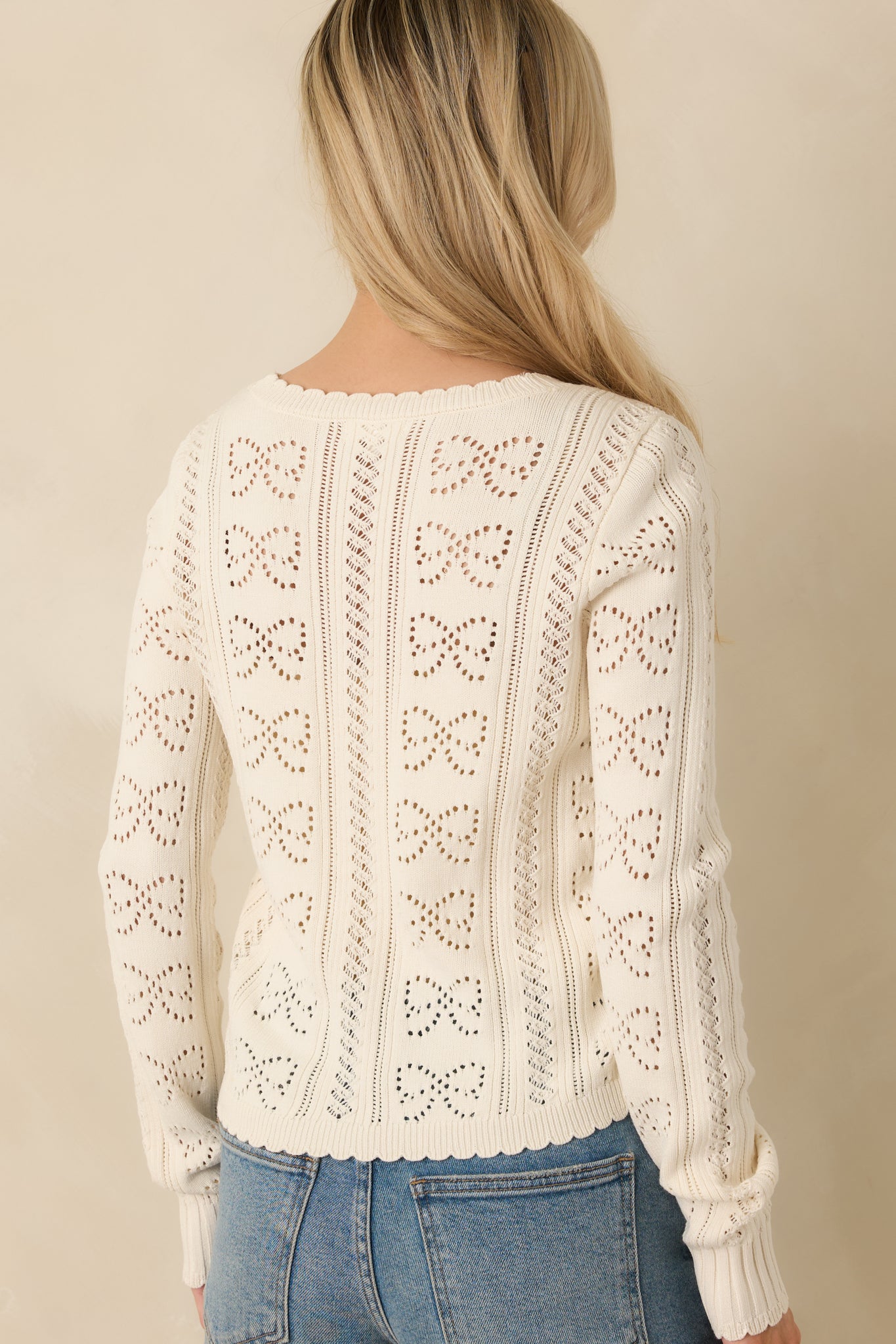 Rear view of the ivory open-knit cardigan showing continuous bow motifs and a smooth, fitted finish.