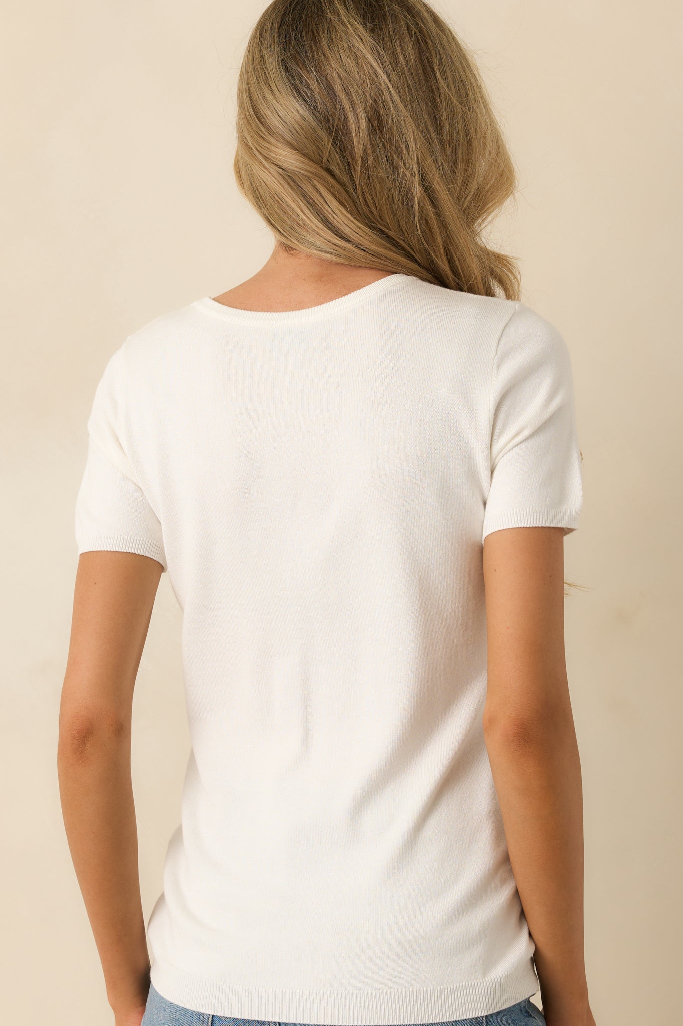 Rear view of the ivory sweater top, showing the ribbed hem, short sleeves, and smooth fabric across the back.