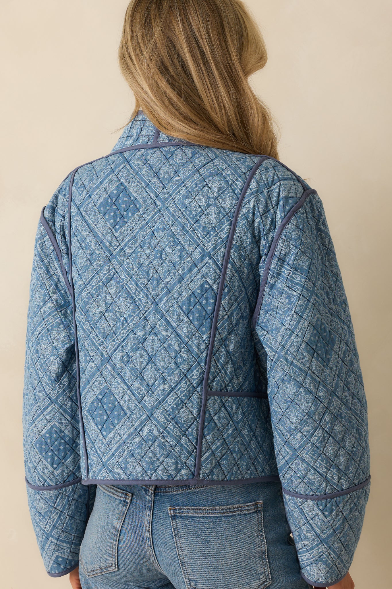 Rear view of the light blue jacket, showing the quilted design, long sleeves, and navy trim accents.