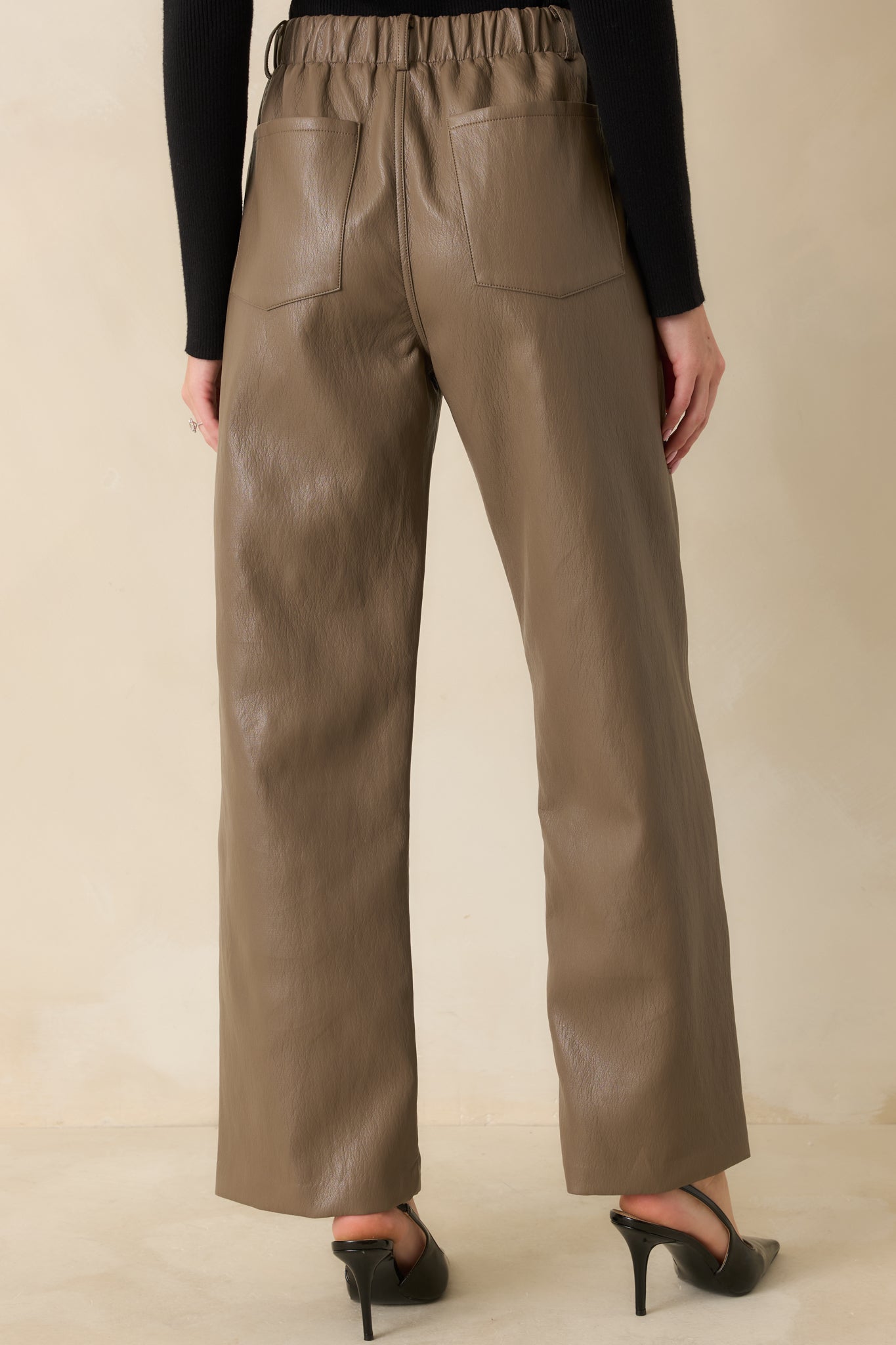 Rear view of the light brown faux leather pants displaying functional patch pockets and straight leg fit.