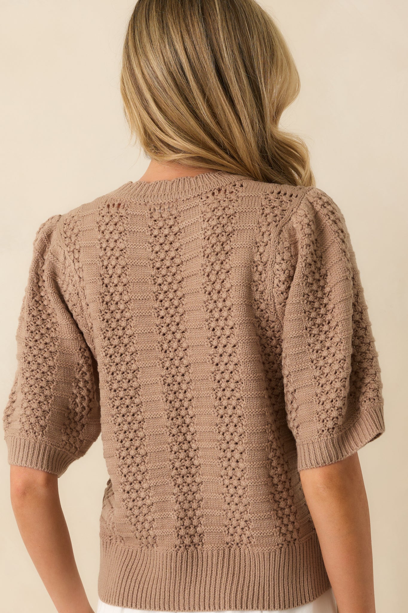 Rear view of the light mocha sweater, showing the consistent vertical panel design, short sleeves, and ribbed hem.