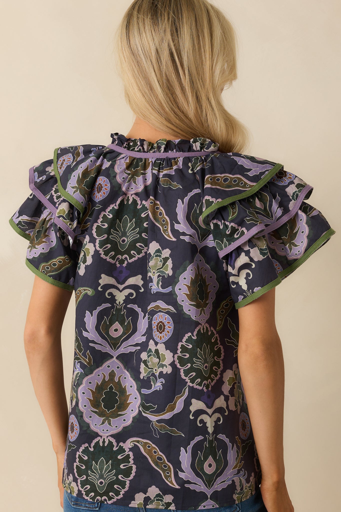 Rear view of navy blouse showing relaxed fit, short ruffle sleeves, and multicolor print extending across the back.